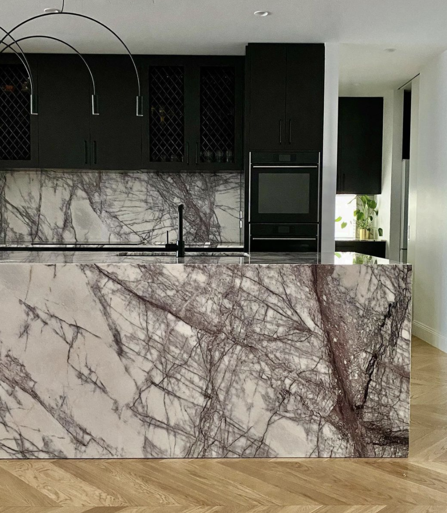 Veined natural-stone kitchen island with dark cabinetry and timber flooring.