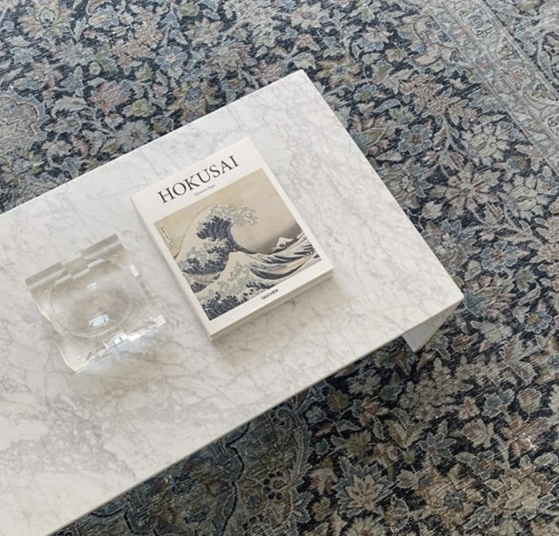 Stone coffee table with books on a richly patterned rug.