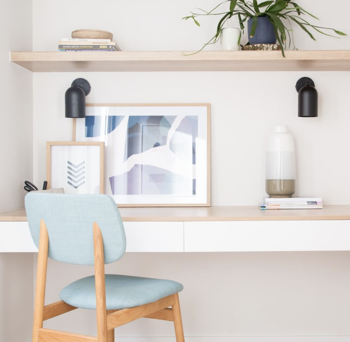 Built-in home workspace with timber shelves, a blue chair and wall-mounted lights.