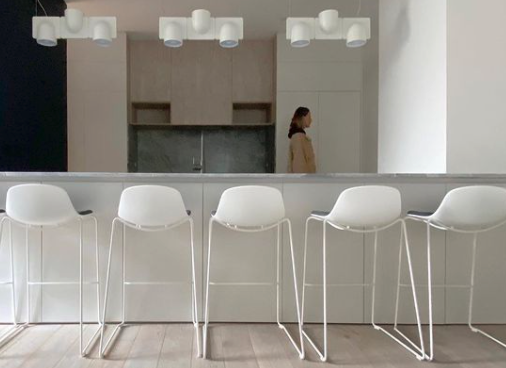 Pale kitchen island with white stools, timber flooring and decorative pendant lighting.