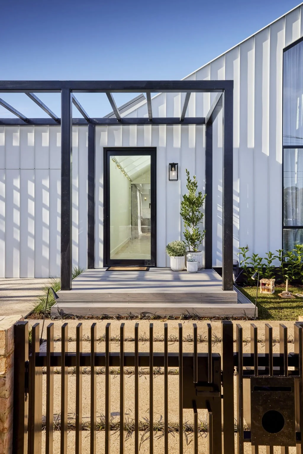 Contemporary entrance with vertical cladding, a black pergola and timber gate.