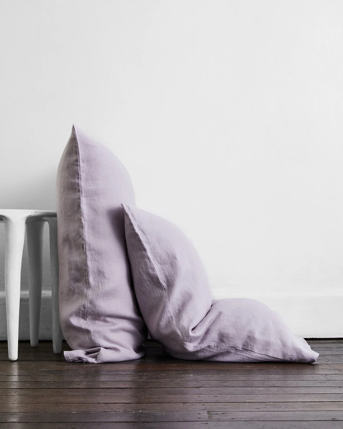 Two lilac linen pillows by Bed Threads resting on dark timber floorboards.