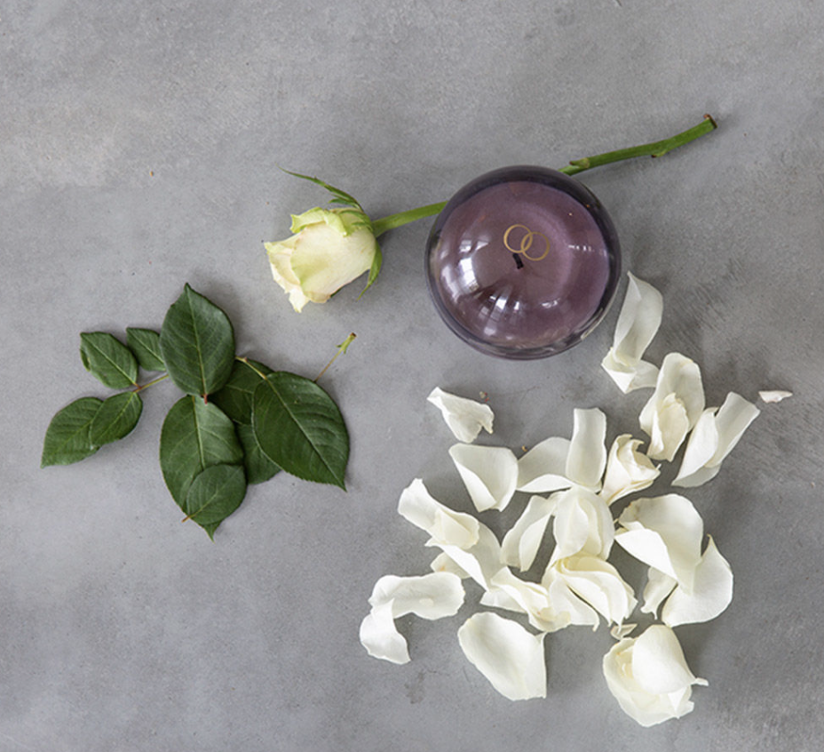 Purple spherical glass candle vessel by Only Orb beside a white rose and scattered petals.
