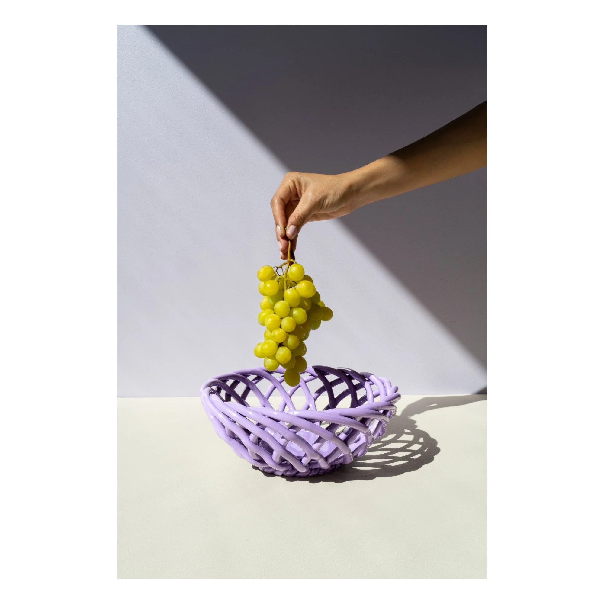 Lilac Sicilia ceramic bowl by Octaevo with an open lattice form and green grapes.