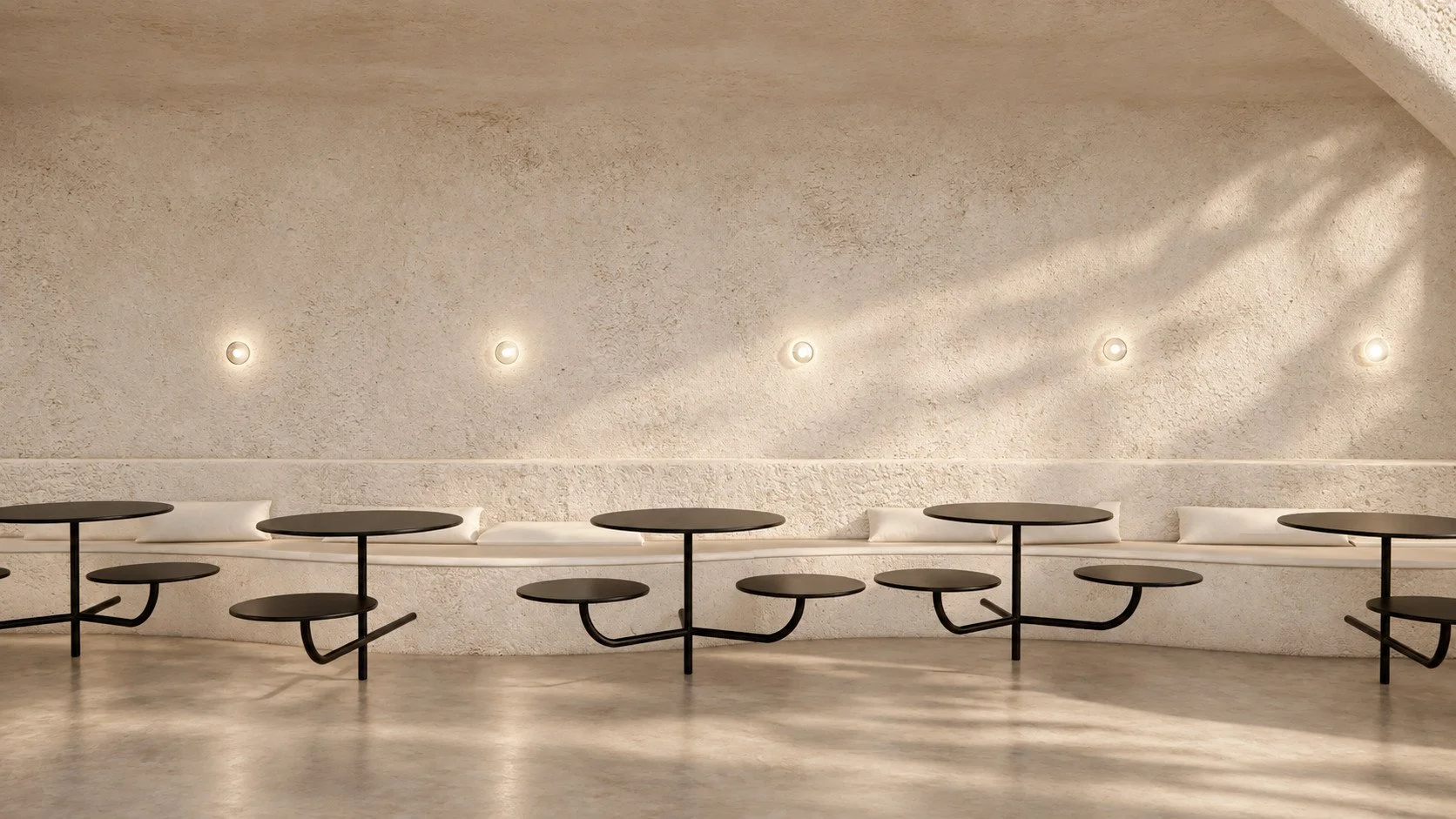 continuous upholstered seating and black table-and-seat forms create a measured rhythm beneath small circular wall lights.