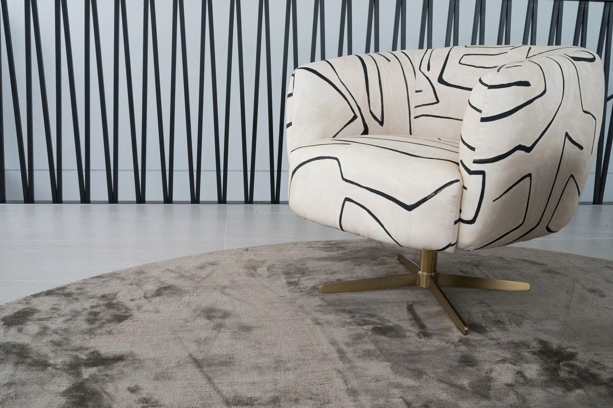 A modern, upholstered armchair with a black abstract line pattern on cream fabric, sitting on a beige circular rug in a room with a wall featuring black vertical stripes.