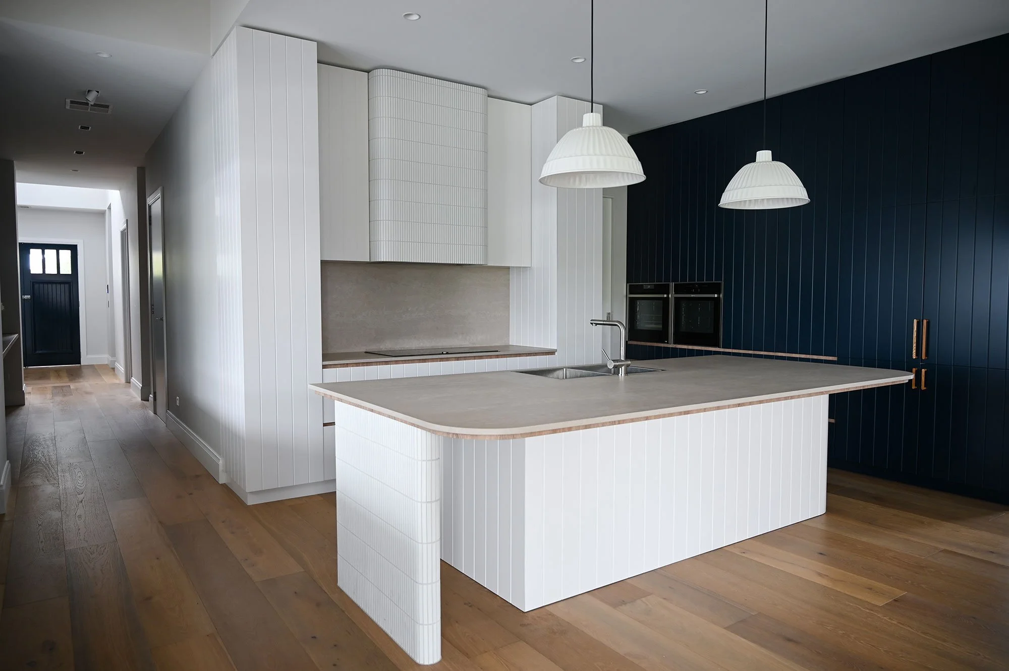 Modern kitchen with white island and blue accent wall, pendant lights, and wooden flooring.