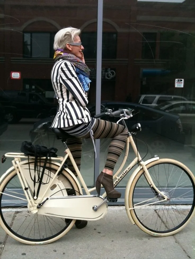 Person in a striped outfit riding a bicycle outside a shopfront.