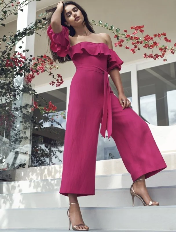 Model wearing a vivid pink jumpsuit beneath flowering branches.