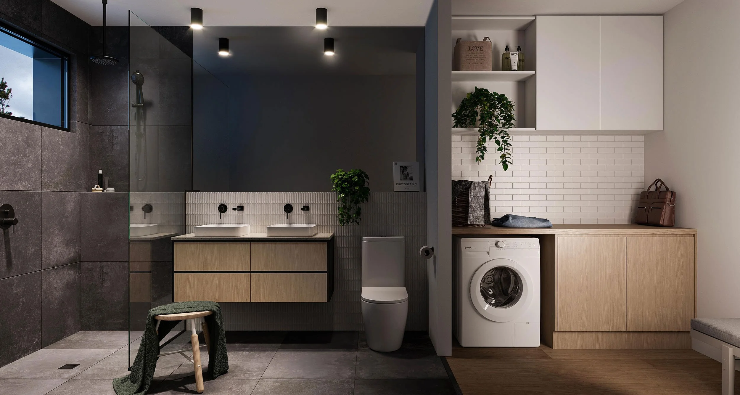 Modern bathroom with dark tiled shower area, dual sinks, and a hidden toilet behind a partial wall. Adjacent laundry area with a washing machine, built-in wooden storage, and decorative items including plants and handbags.