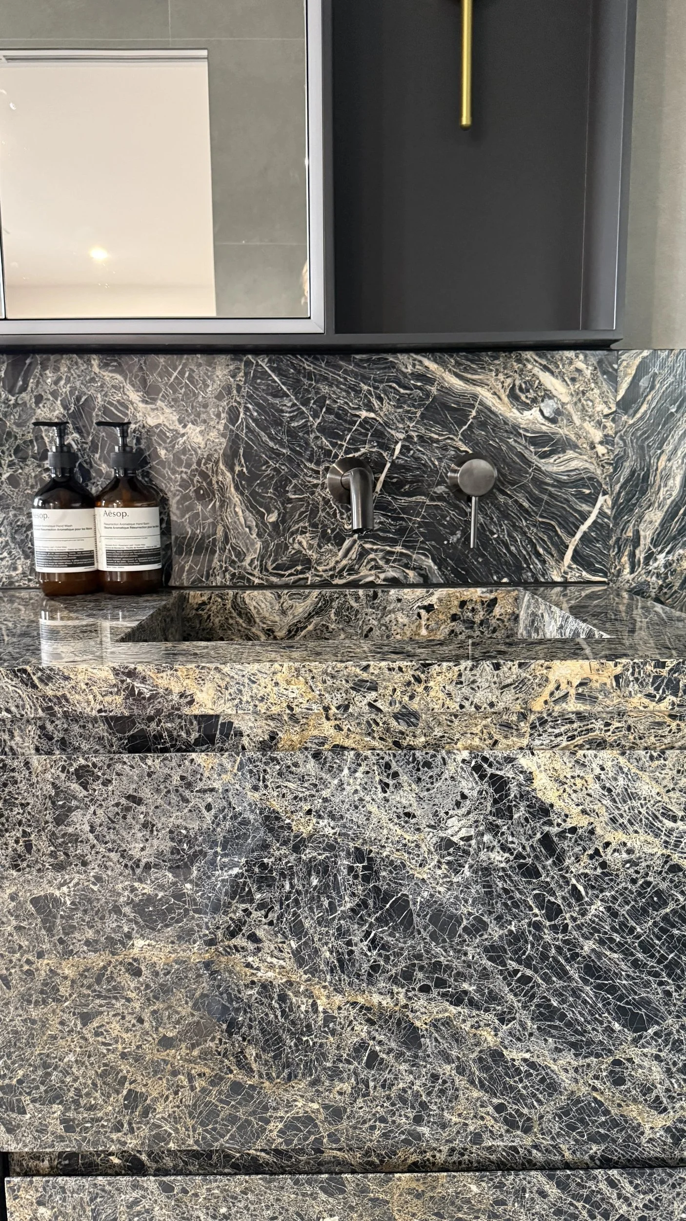 Dark veined stone bathroom splashback with wall-mounted taps and toiletries.