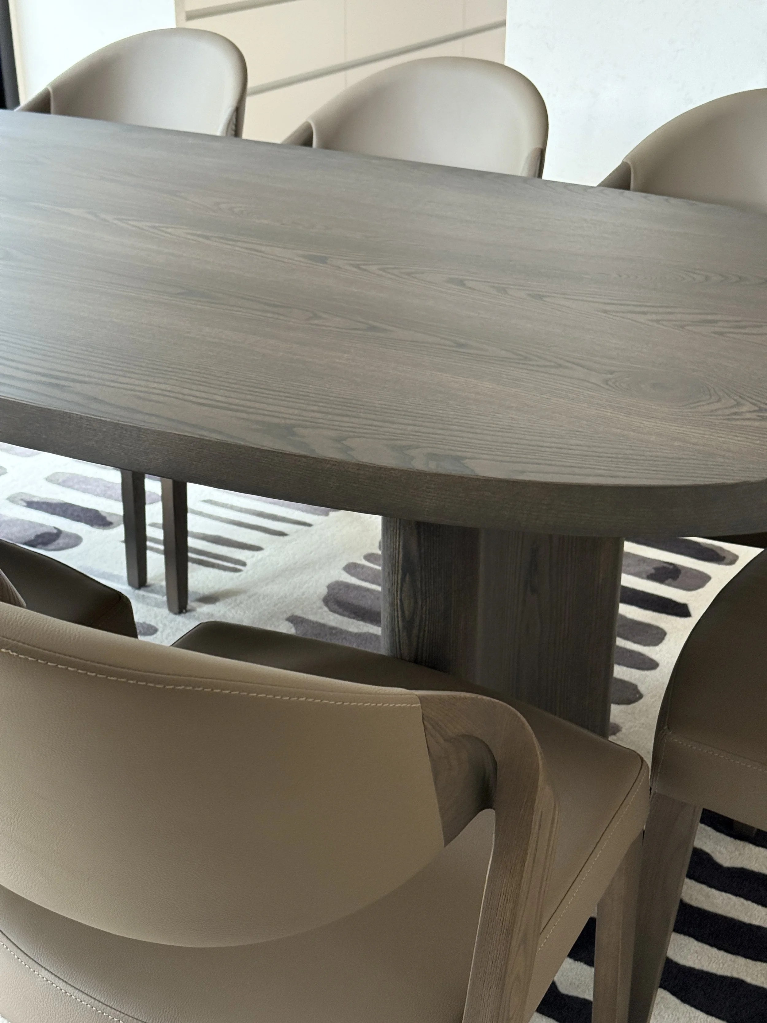 Close-up of a wooden dining table surrounded by beige leather chairs, with a geometric rug underneath.