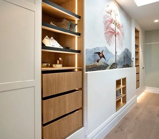 Interior view of a hallway with built-in shelves, a painted mural of nature with a large pink flower and birds, and wooden flooring.
