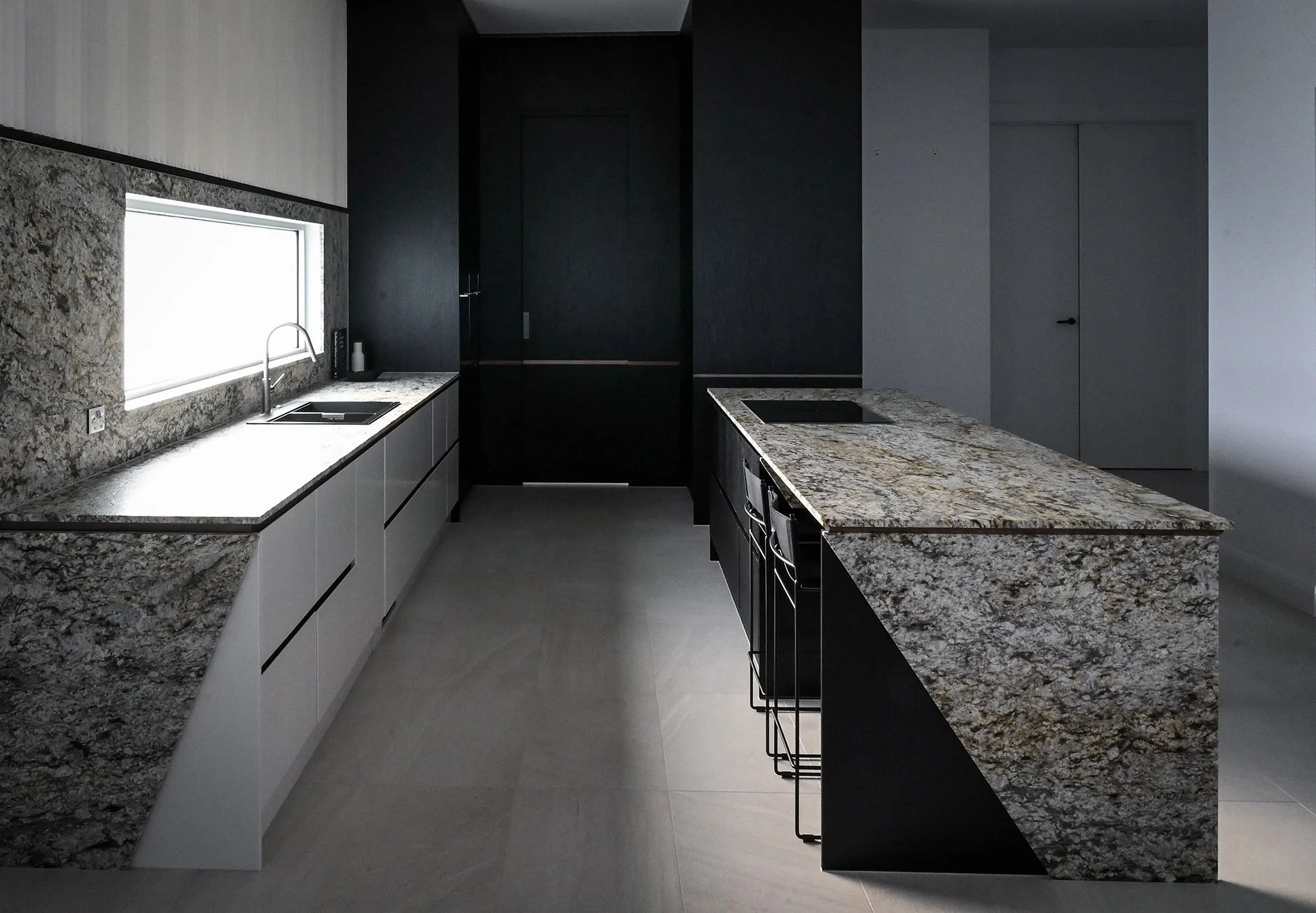 Modern kitchen with granite countertops, black and white cabinetry, a window over the sink, and a minimalist design.