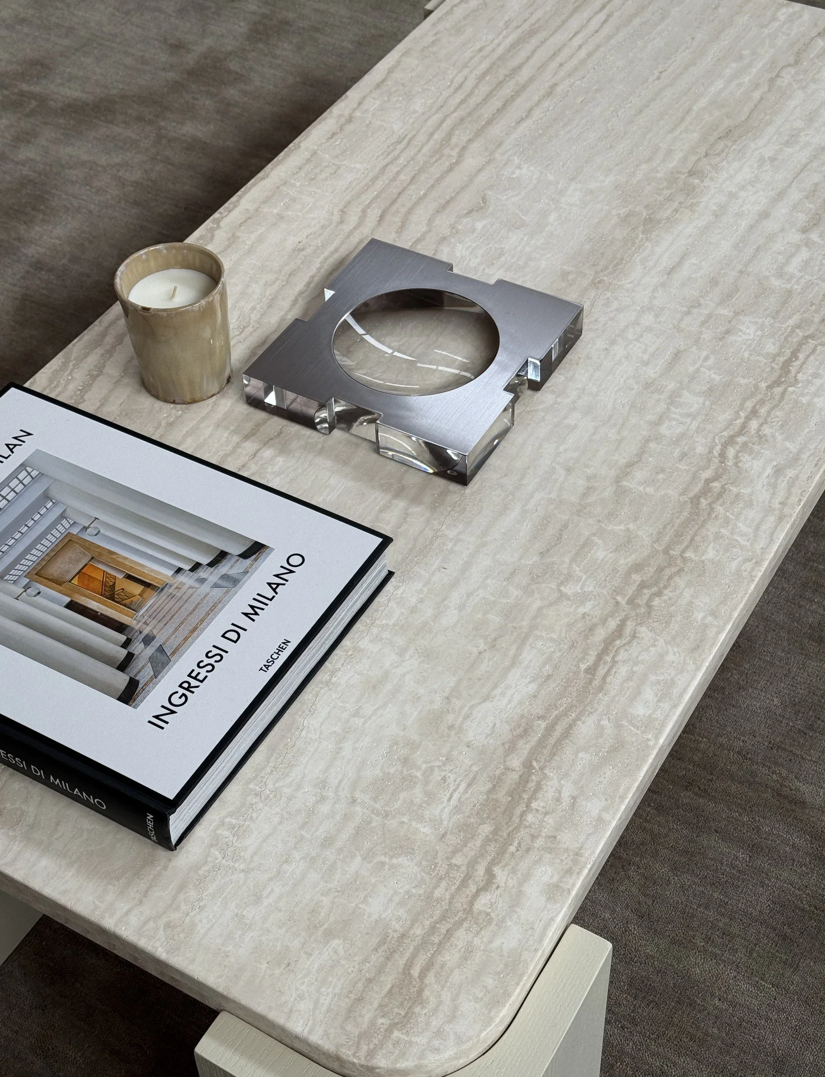 Pale stone coffee table styled with a book, ceramic cup and sculptural metal tray.