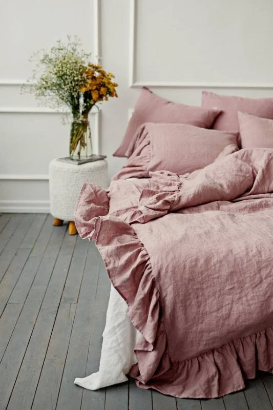 Soft pink bed linen and layered cushions against white wall panelling.