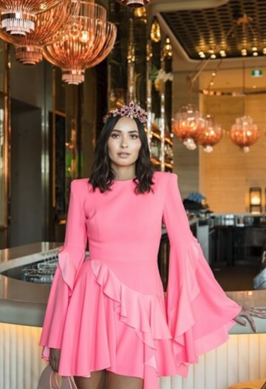 Model wearing a bright pink dress within an ornate interior.