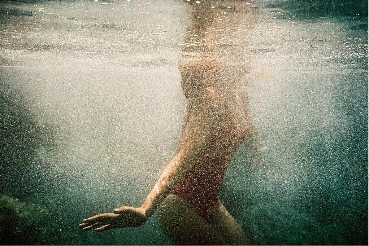 A person swimming underwater, wearing red swimwear, with water bubbles surrounding them.