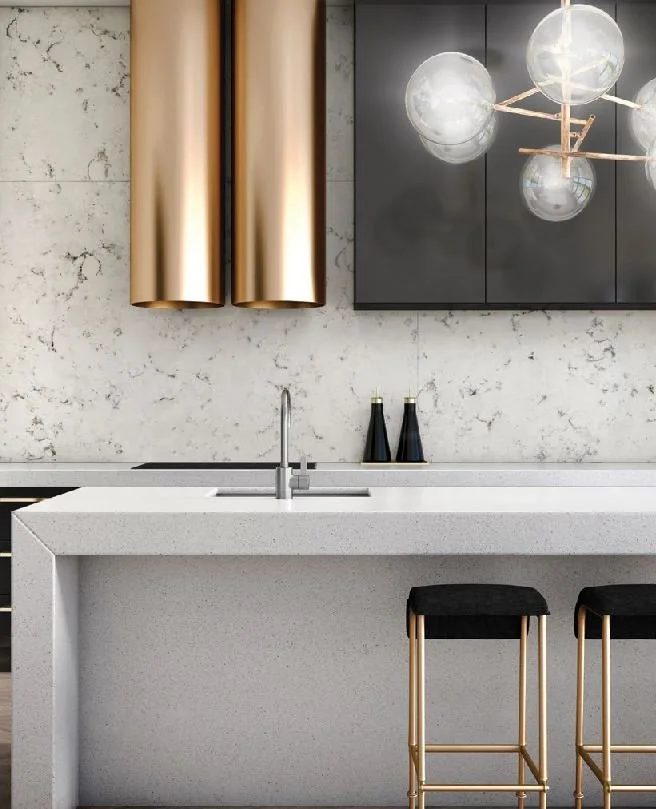 Pale kitchen island beneath decorative lighting with metallic details.