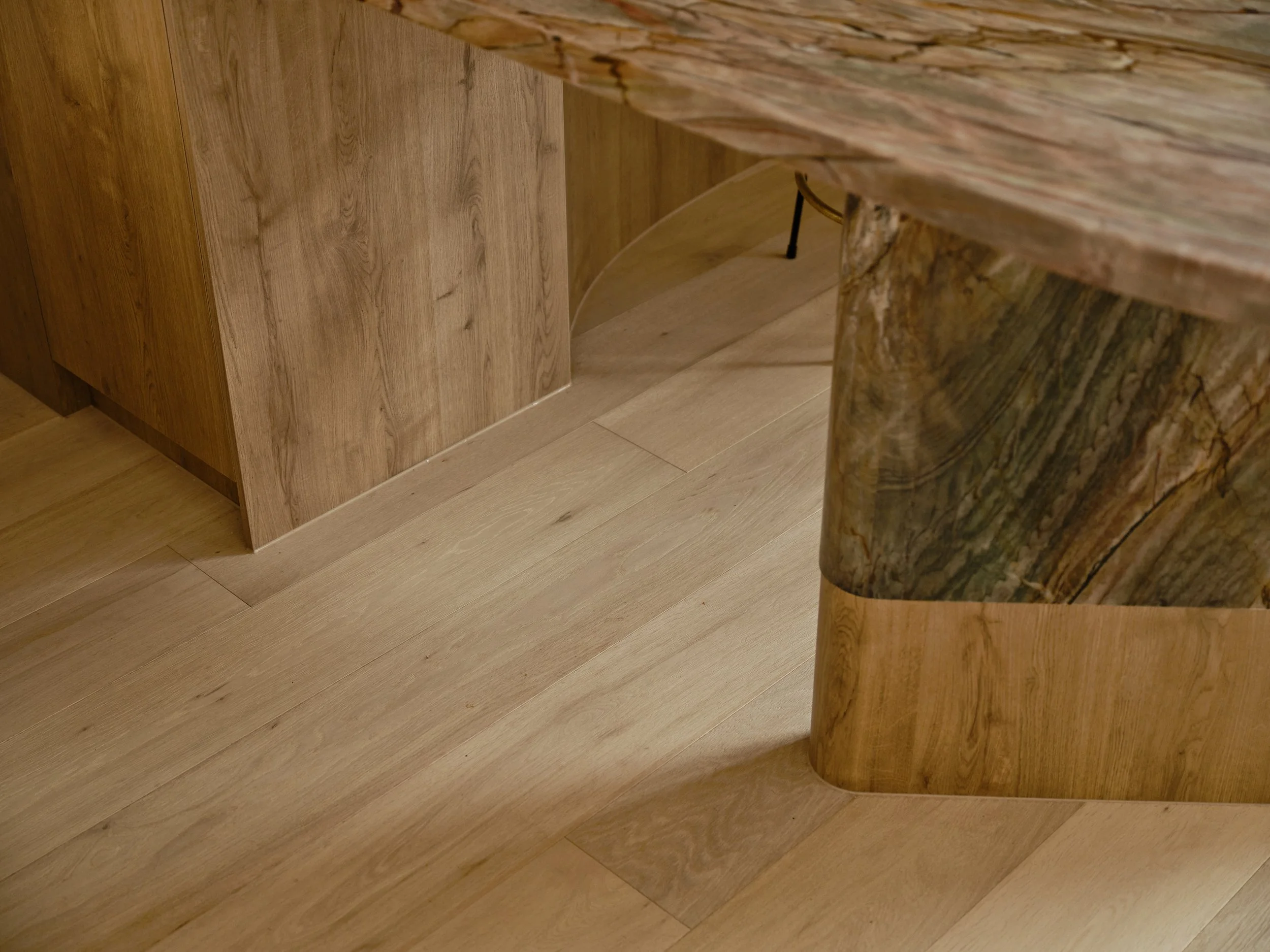 Detail of the richly veined stone kitchen island beside timber cabinetry and pale timber flooring.