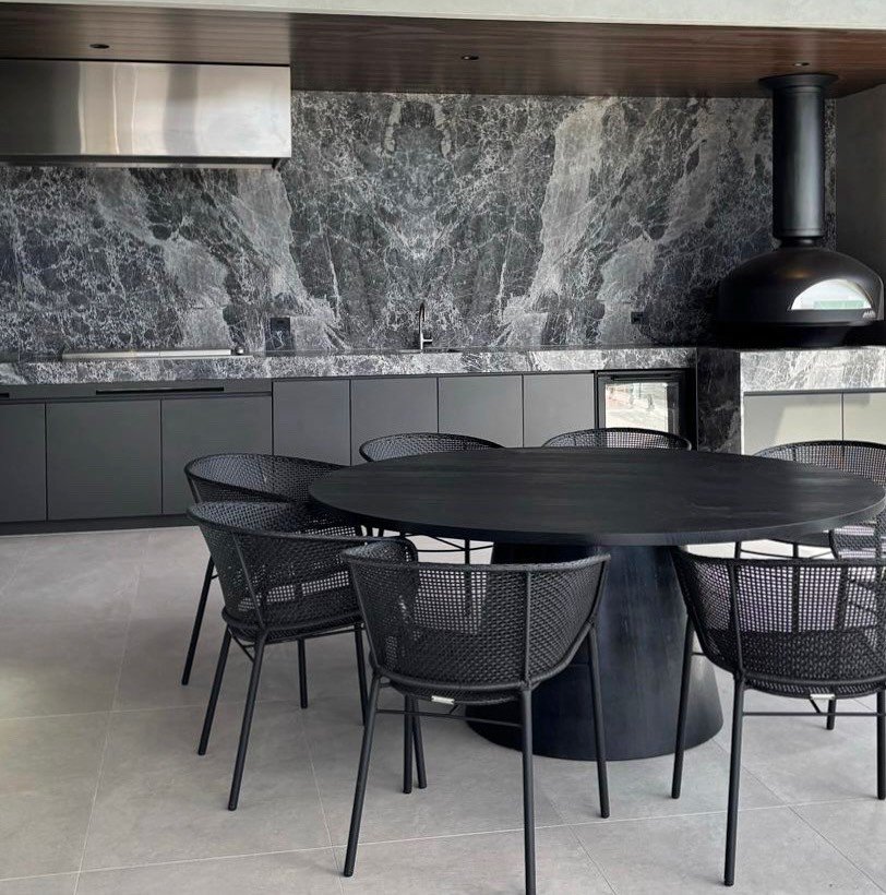 Dining area with a black table and woven chairs against a dramatic veined stone wall and suspended black fireplace.