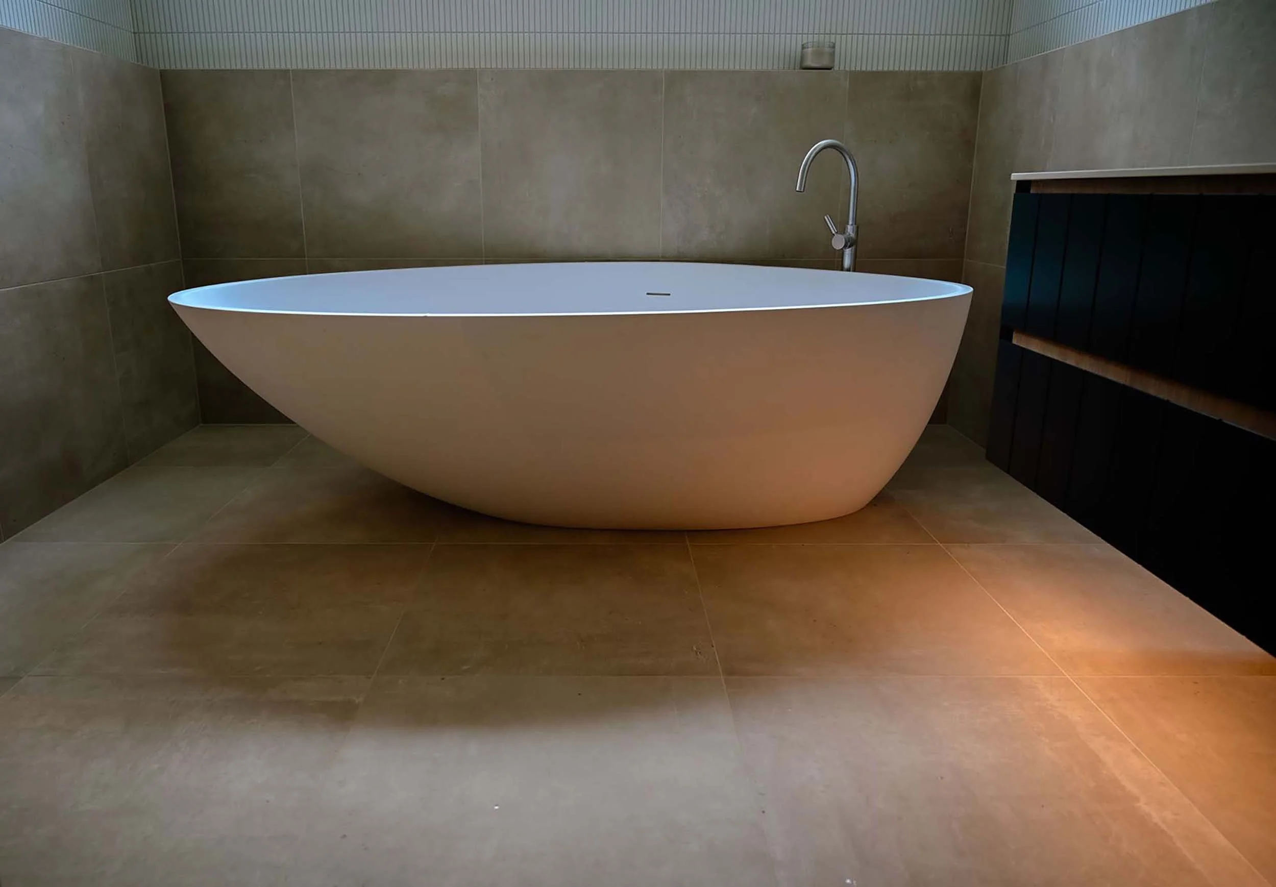 Modern bathroom with a freestanding bathtub, brown tiled walls, and floor, and a black cabinet on the right side.