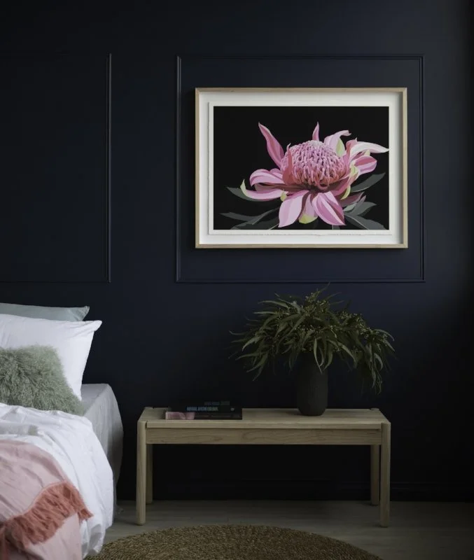 Pink botanical artwork above a bedside table against dark wall panelling.