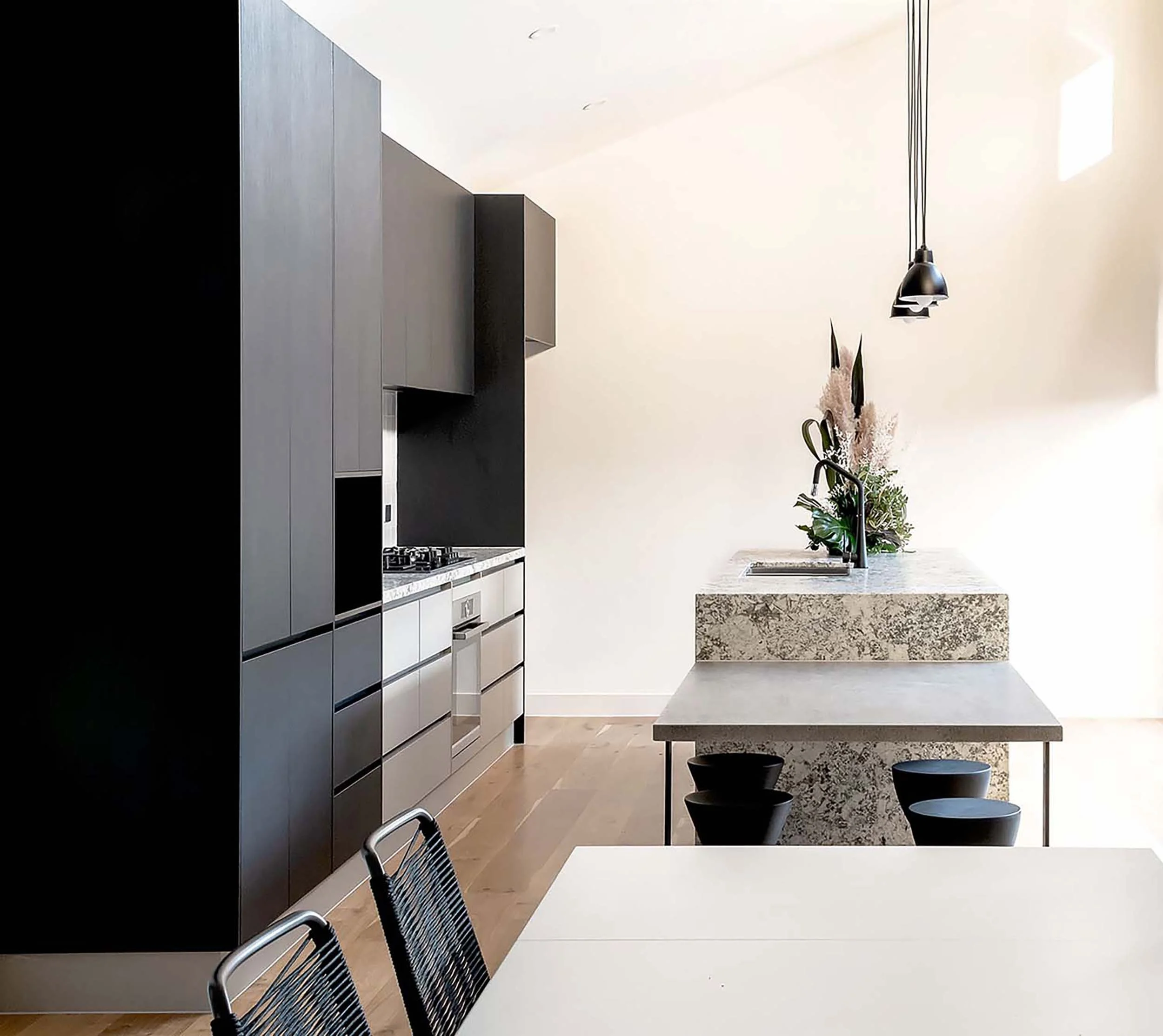 Modern kitchen with gray cabinetry, a marble island, pendant lights, and a vase with flowers.