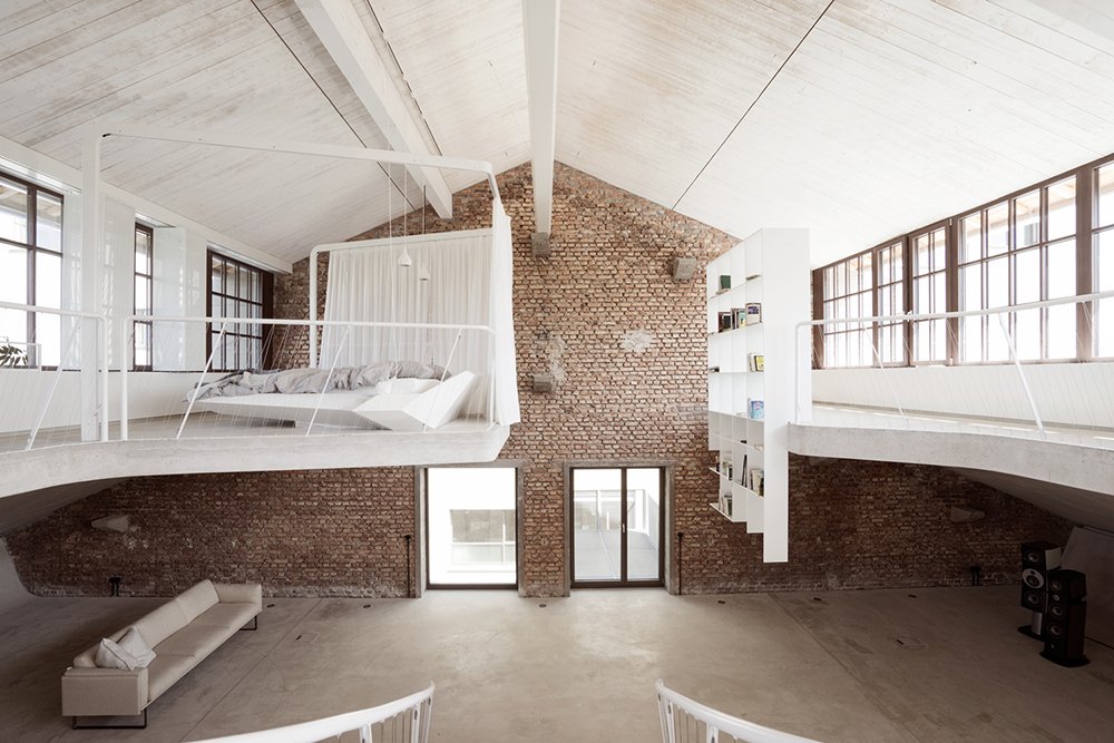High-ceilinged interior with exposed structure, tall windows and pale furnishings.