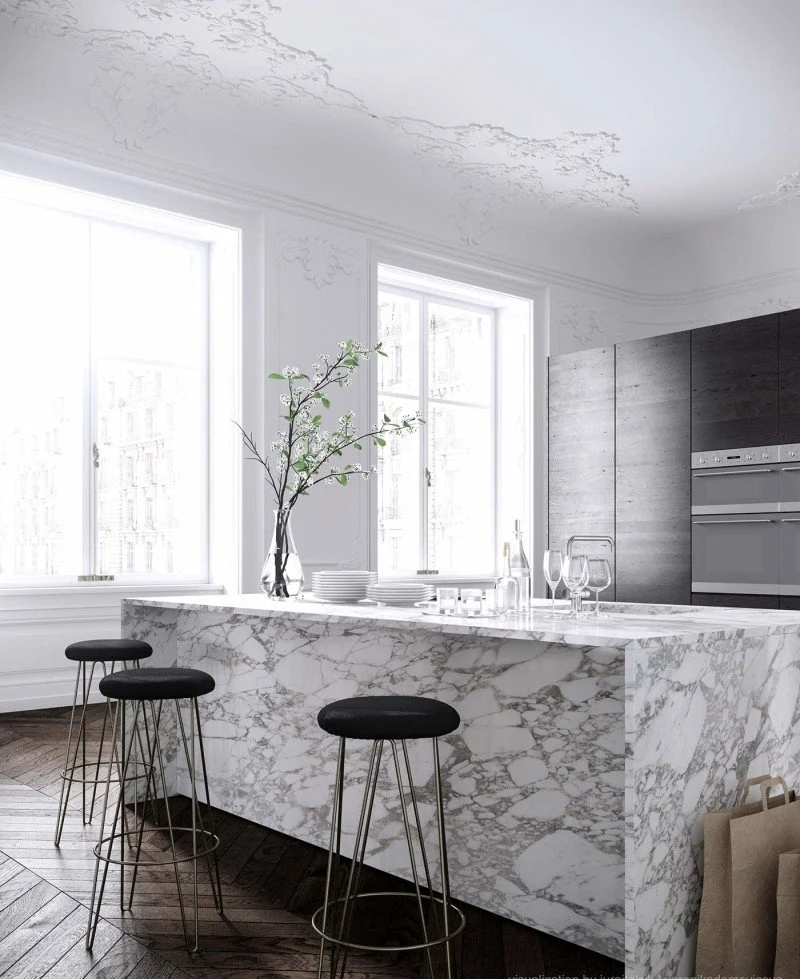 Kitchen with a strongly veined stone island and dark stools beside a bright window.
