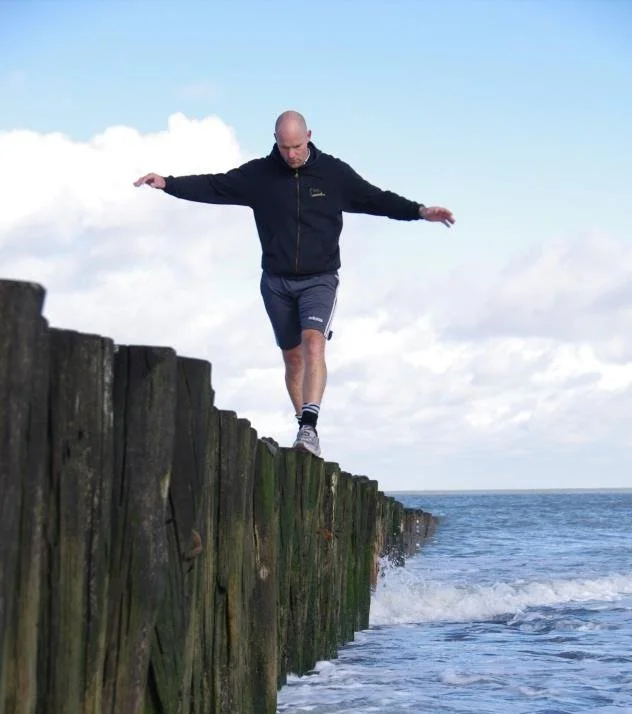 Person balancing on wooden posts by the sea