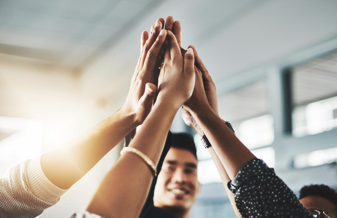 A group of people joining hands in a high-five gesture indoors, symbolizing teamwork and success.