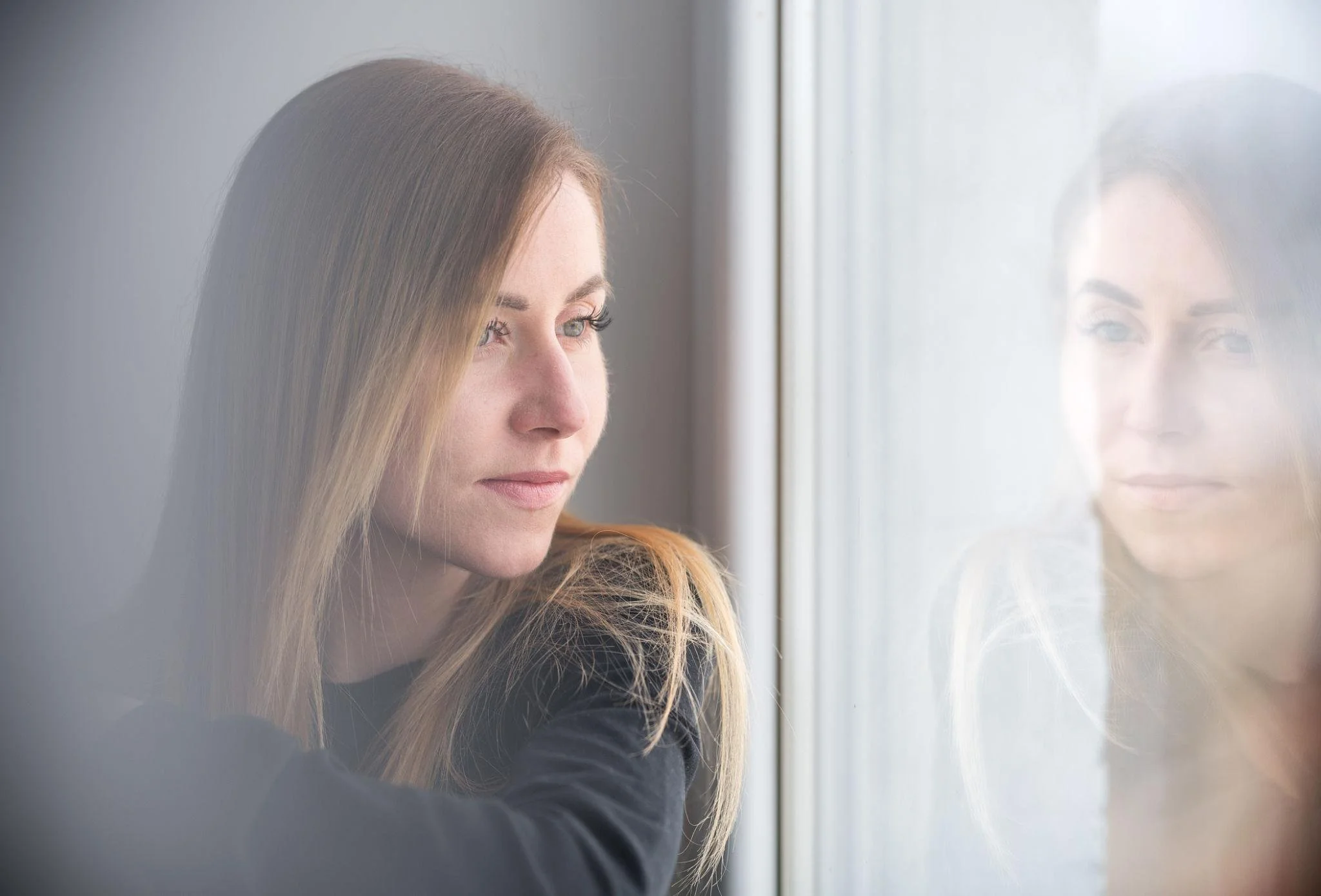 ADHD woman after EMDR finding calm in her storm as she stares out the window into her reflection.