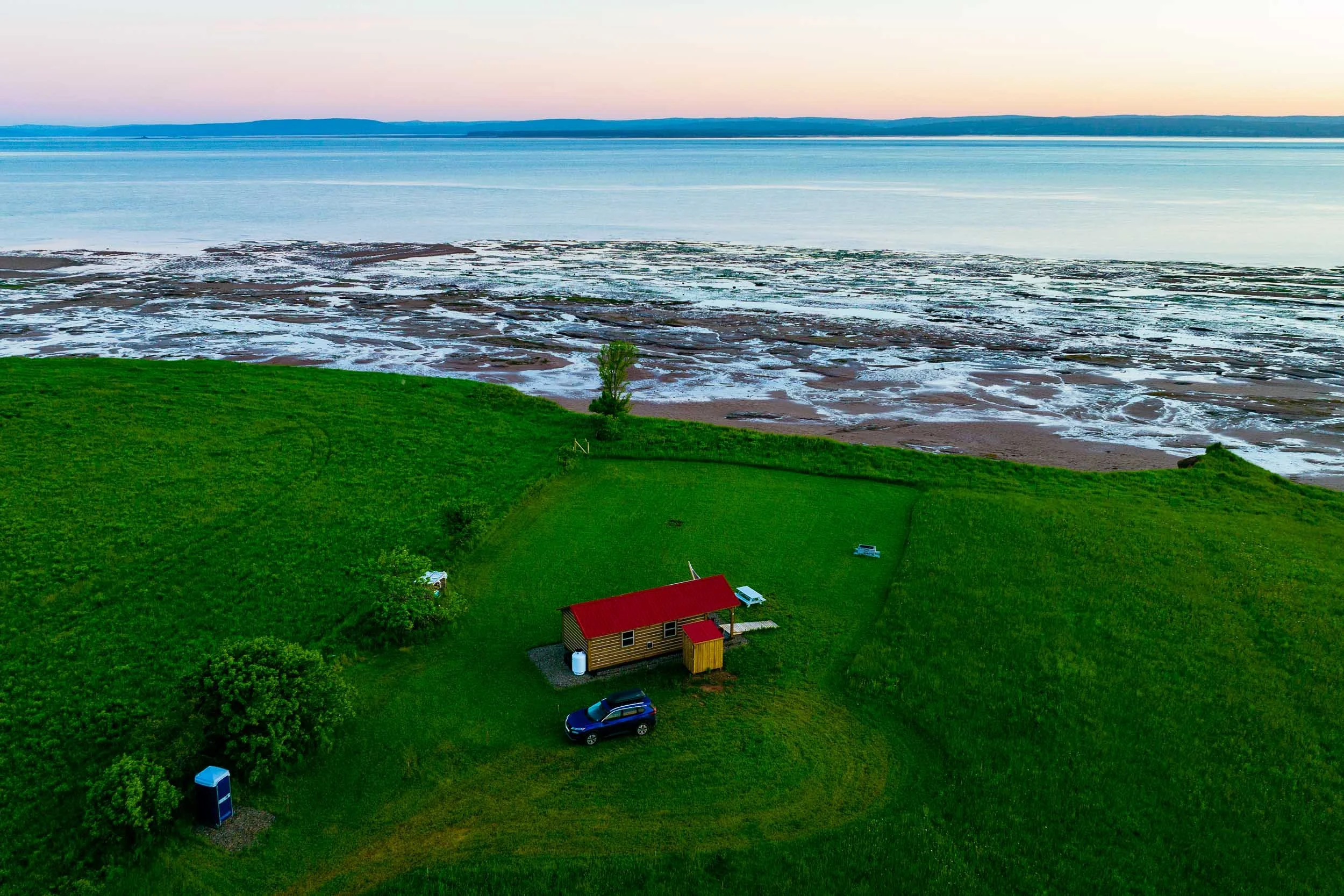 Cabin with red roof on lush green grass beside the coast while tide is out.