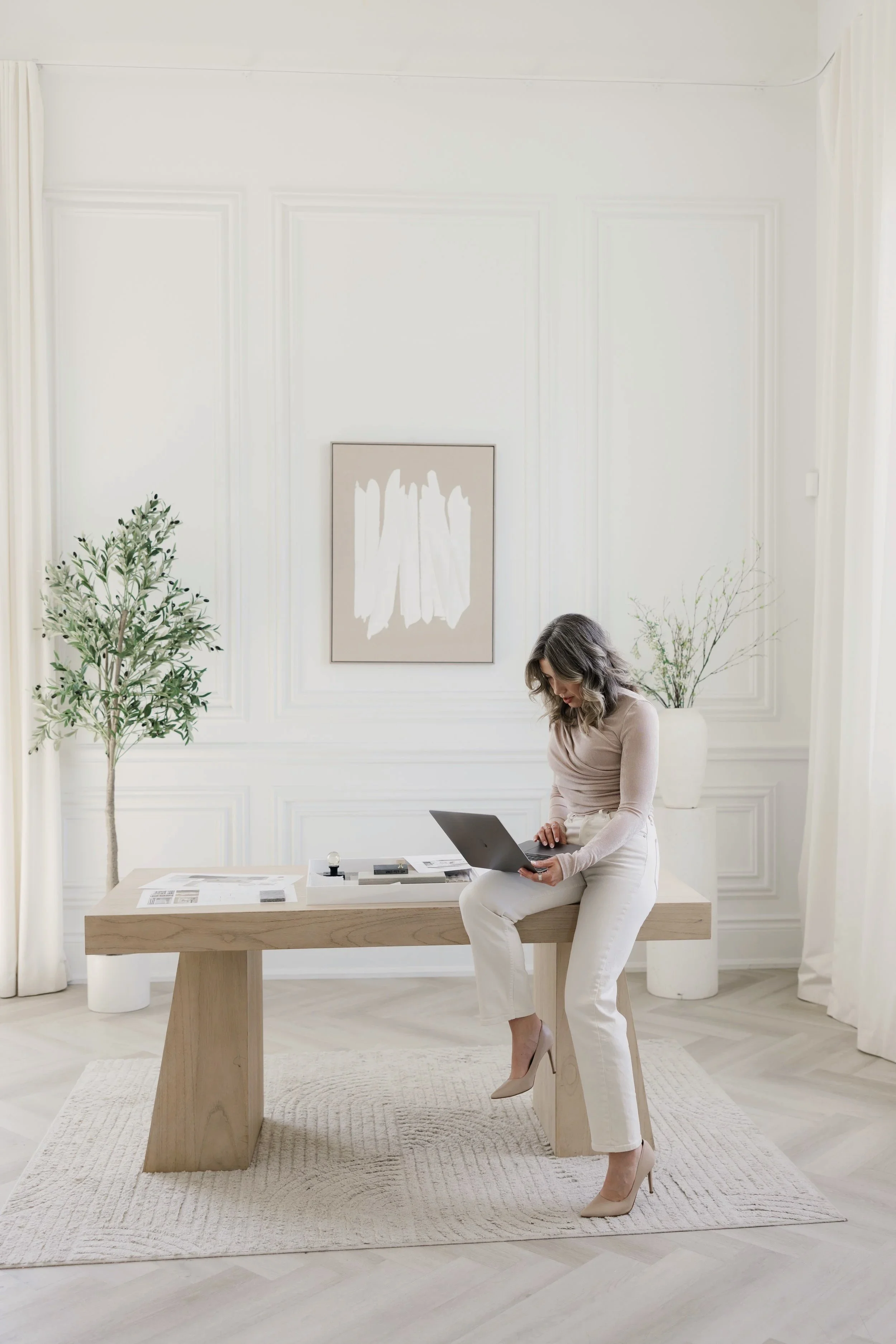 Leah Simpson on her laptop during a virtual design session, with material samples on an oak table