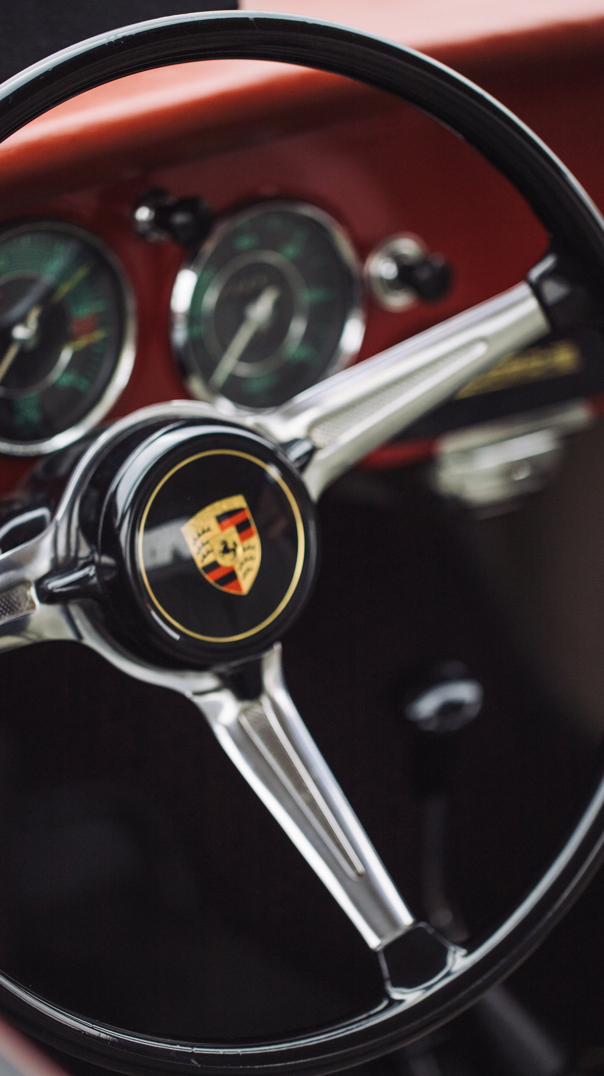 Close-up of a vintage Porsche steering wheel with a black center logo and a dashboard with gauges in the background.