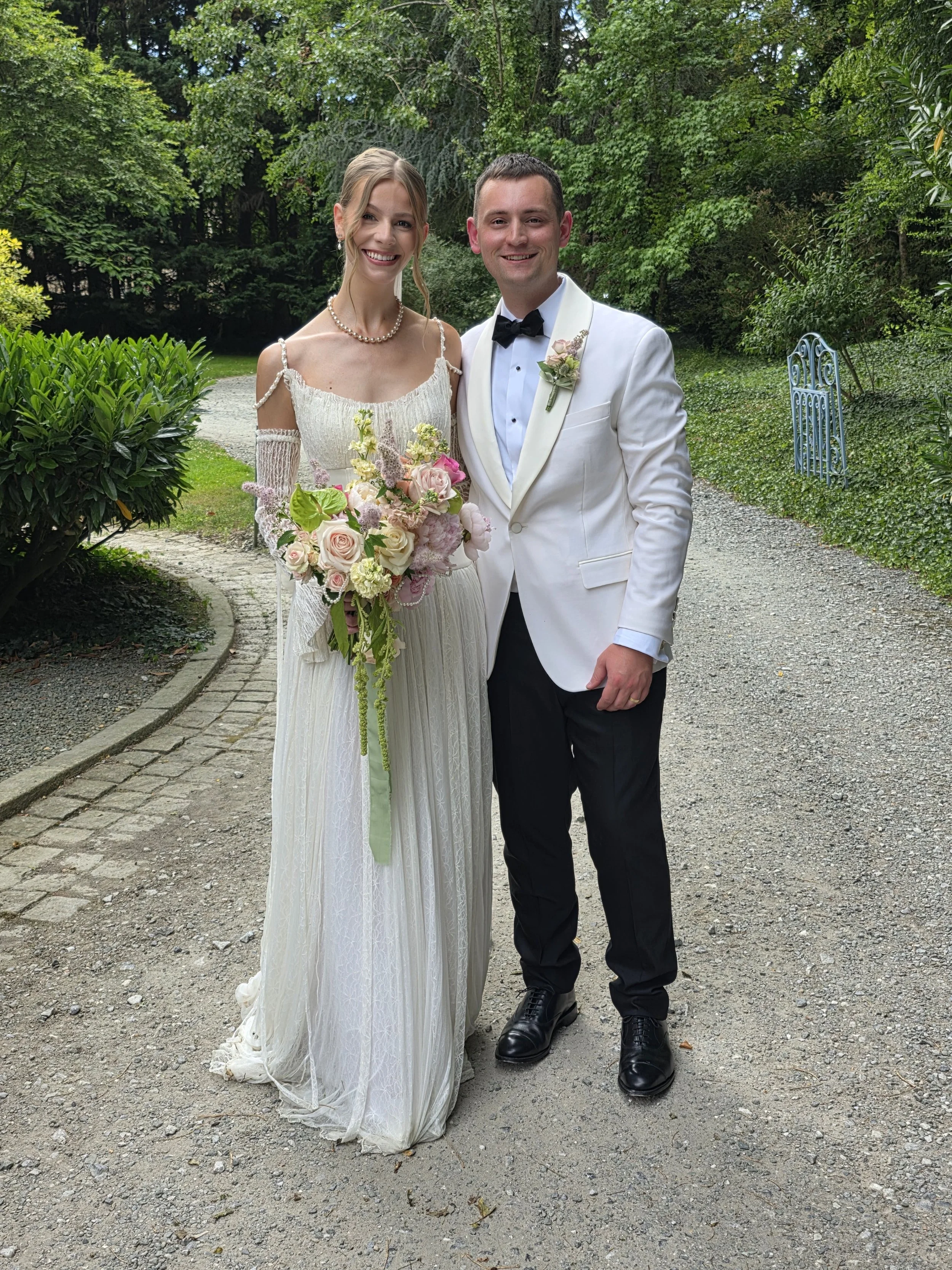 The happy couple bride and groom smile for the camera and the bride is holding her floral bouquet at a chateau in france for a wedding celebration