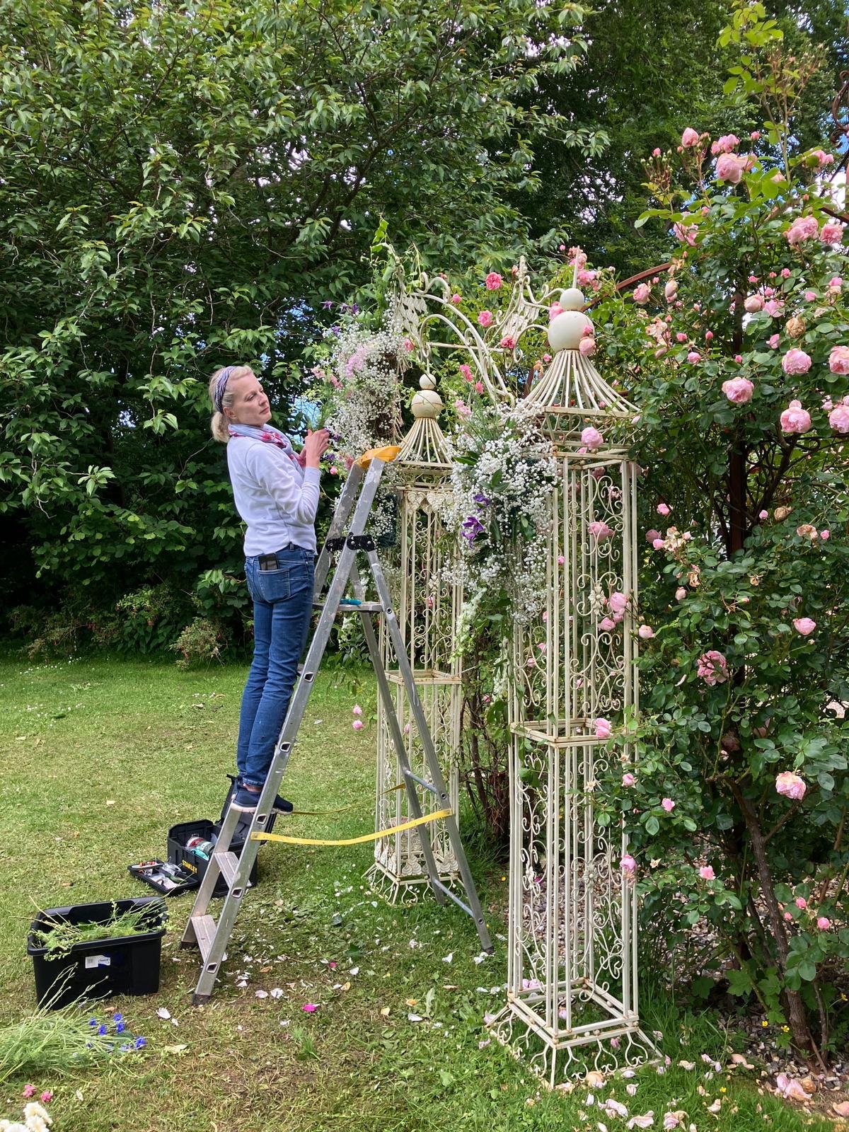 woman florist standing on a ladder in France creating a floral arch for an outdoor wedding at a chateau