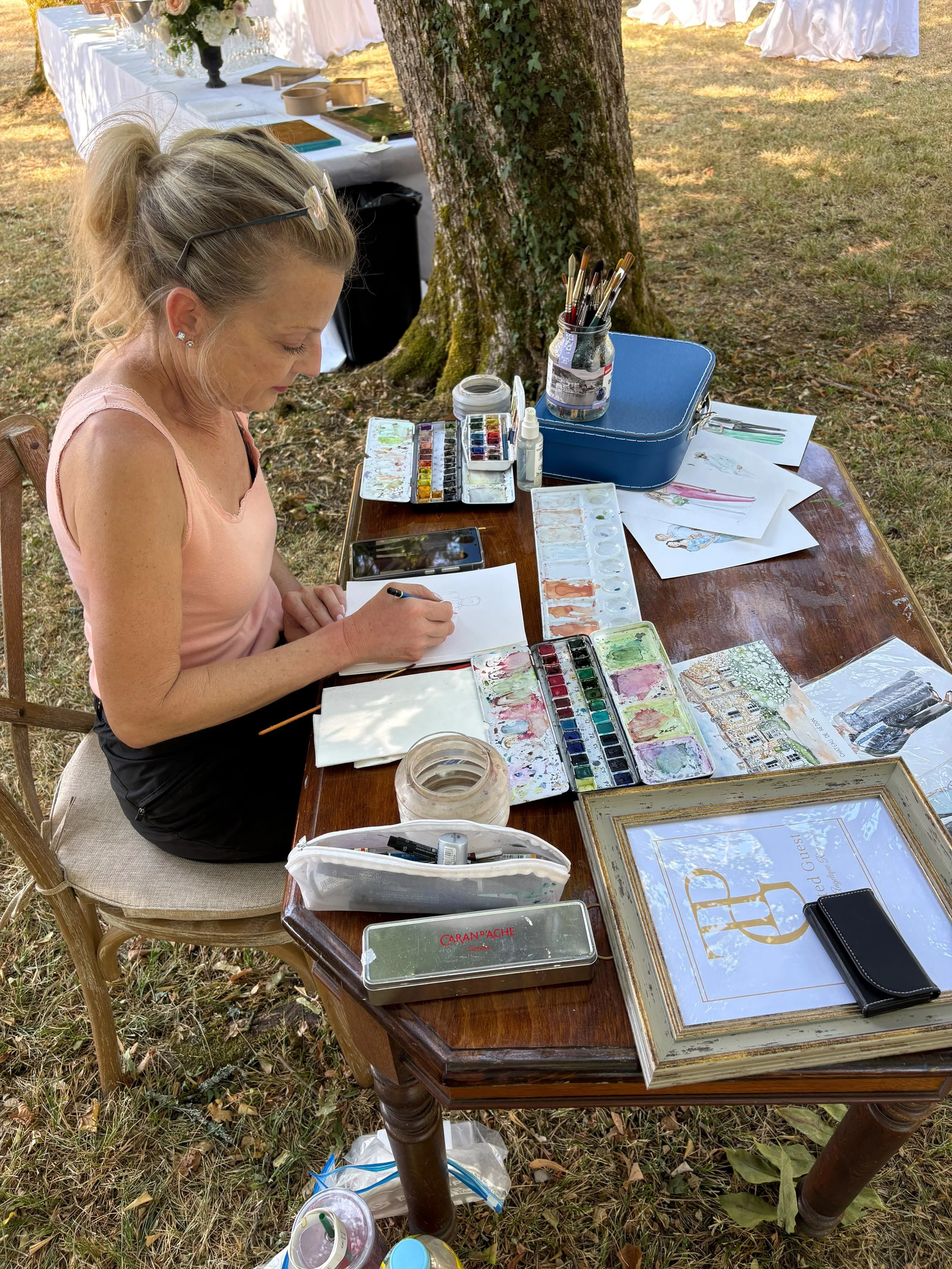 woman sits at a table painting portraits of wedding guests at a wedding in Southwest France Dordogne after creating the wedding florals for their wedding.