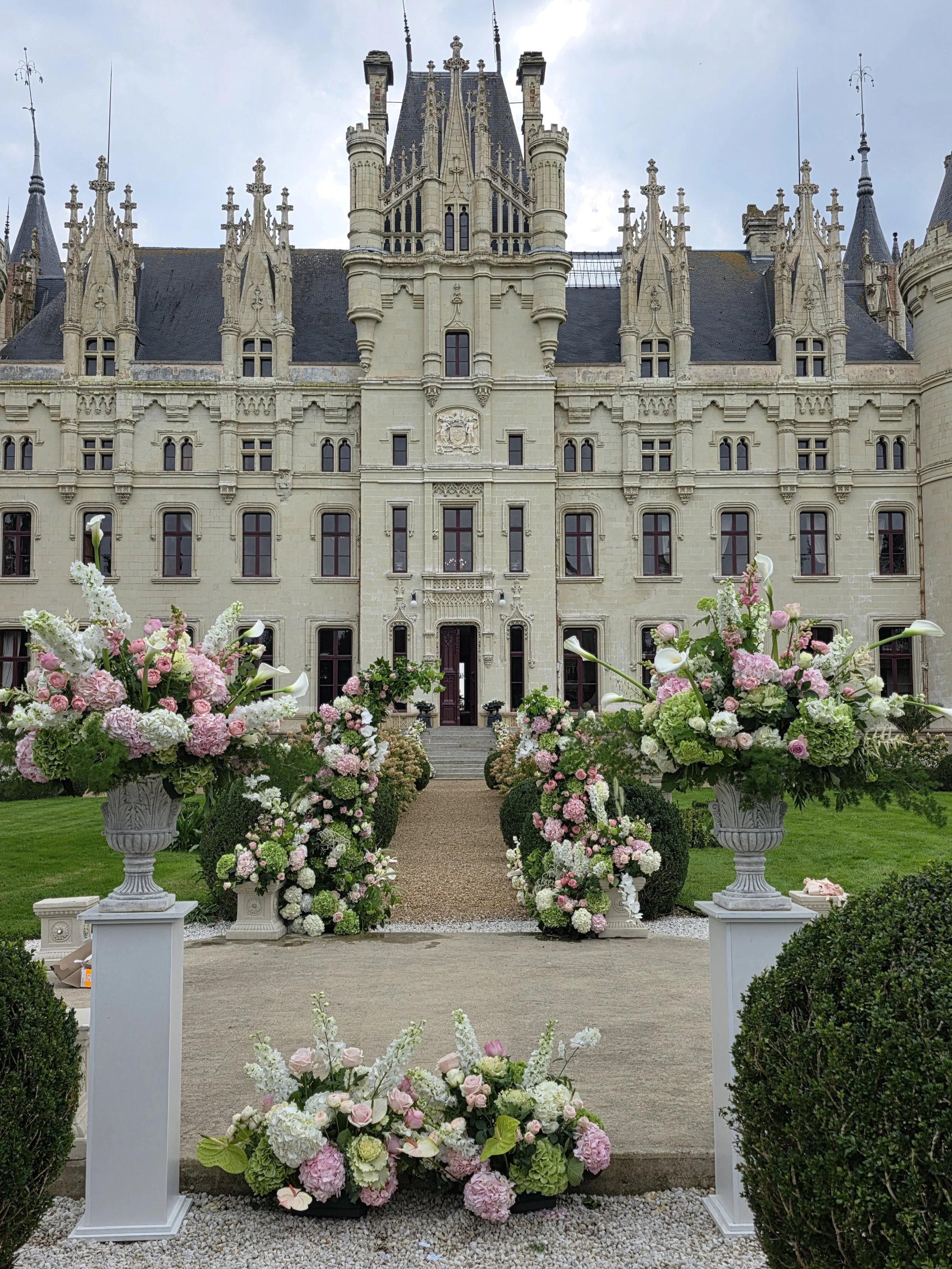 a castle front with pink and green wedding flowers waits for a wedding couple for their destination wedding in france