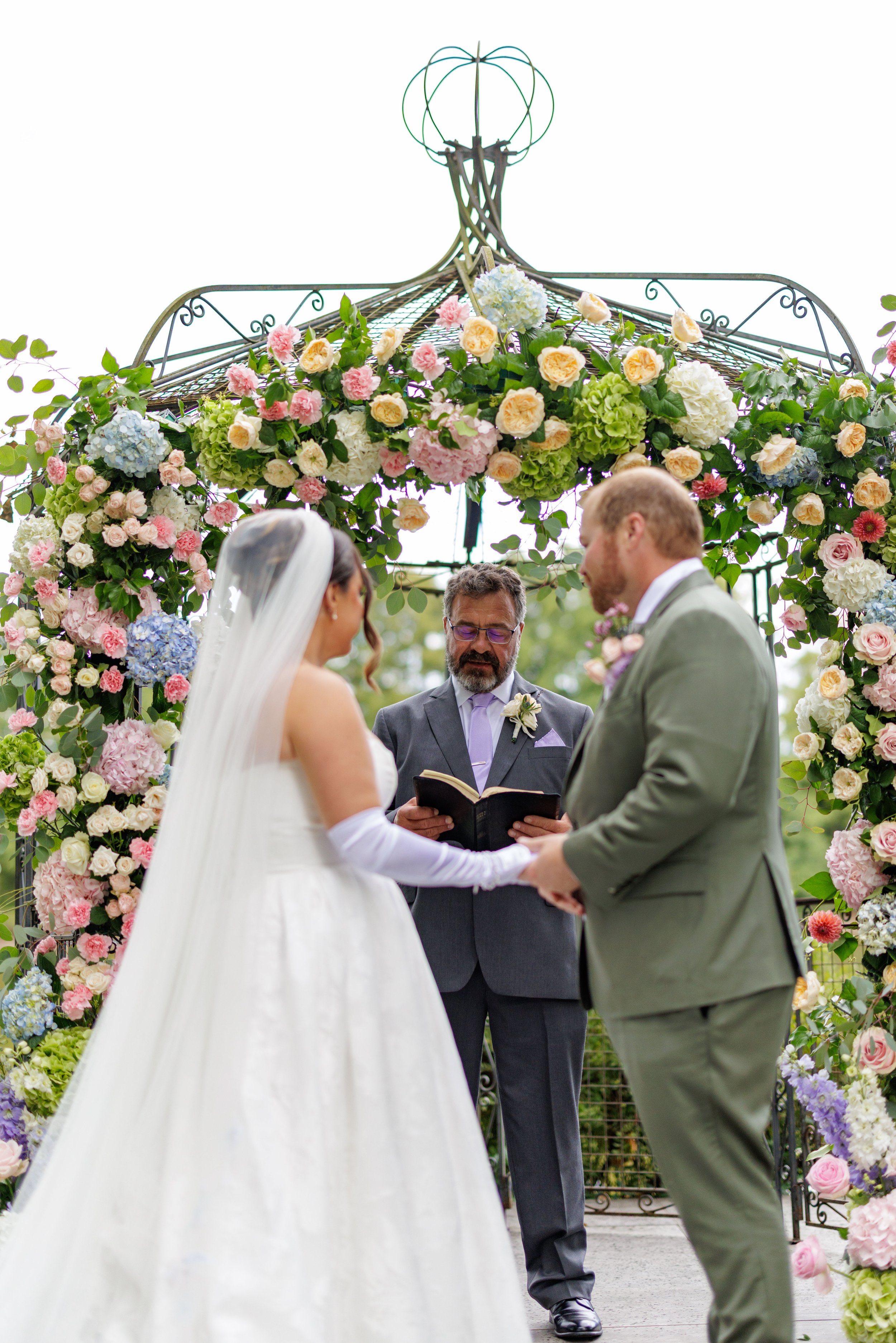 bride and groom stand in front of an officiant for their destination wedding in france before a garden inspired floral arch.