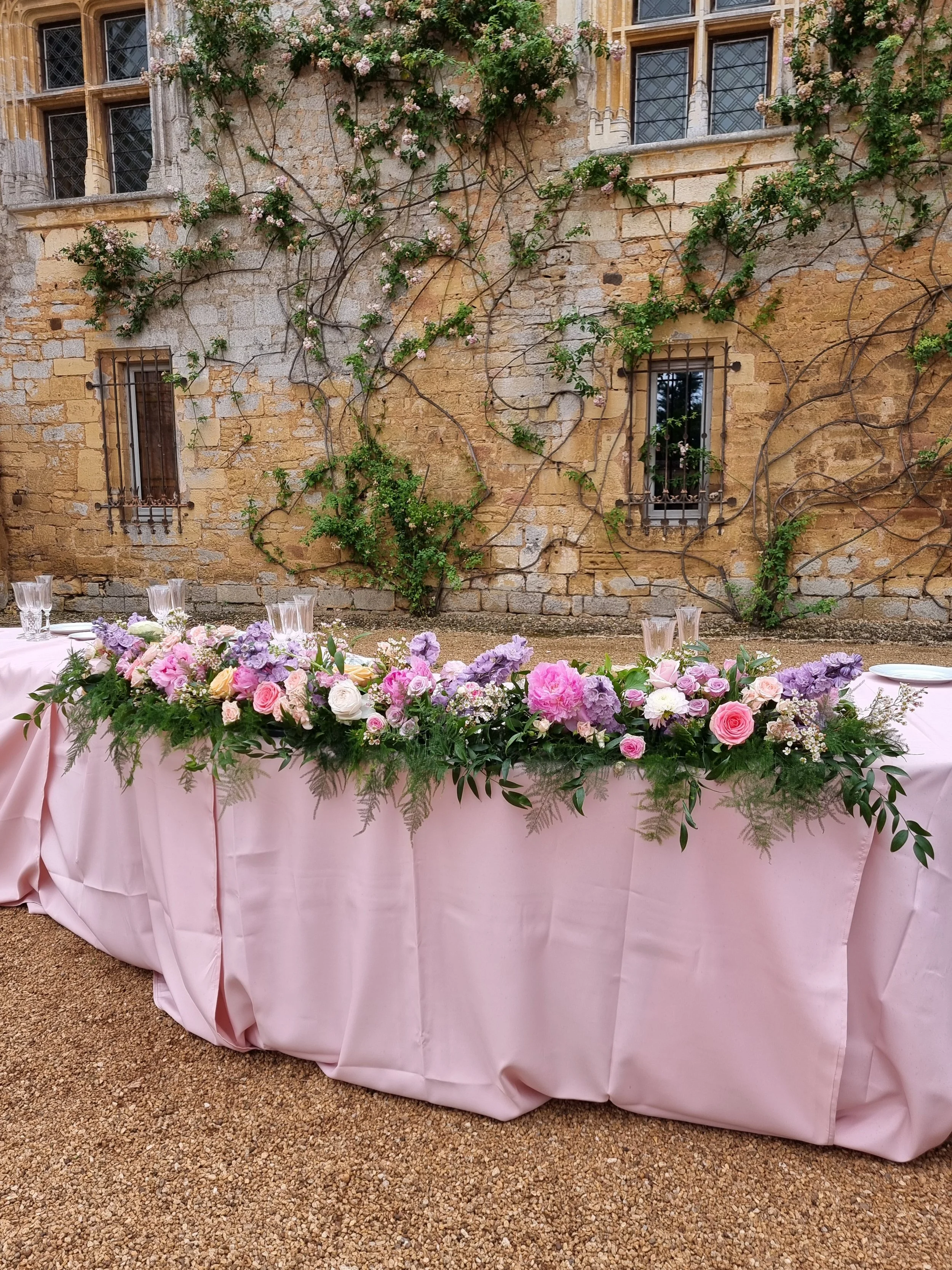 a wedding dinner table for the honored guests and pink and violet flower arrangements on the center facing guests.