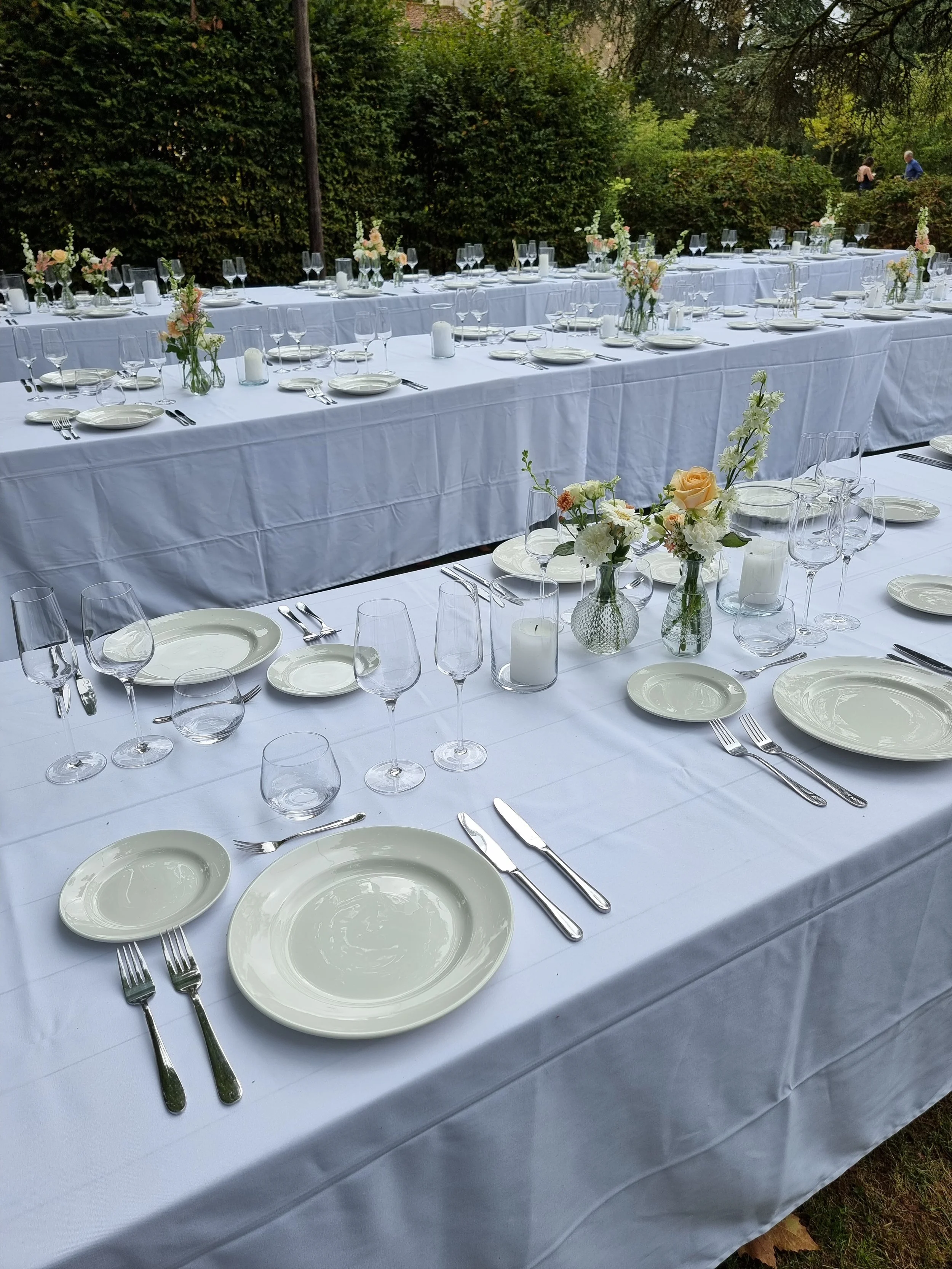 table dressed in white linen with plates and cutlery and simple bud vases of peach and white flowers