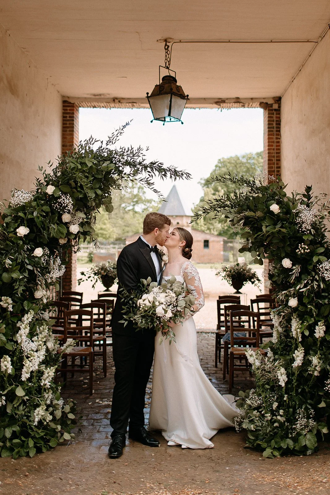 bride and groom kiss under a green and white floral arch at a chateau in france for their destination wedding.