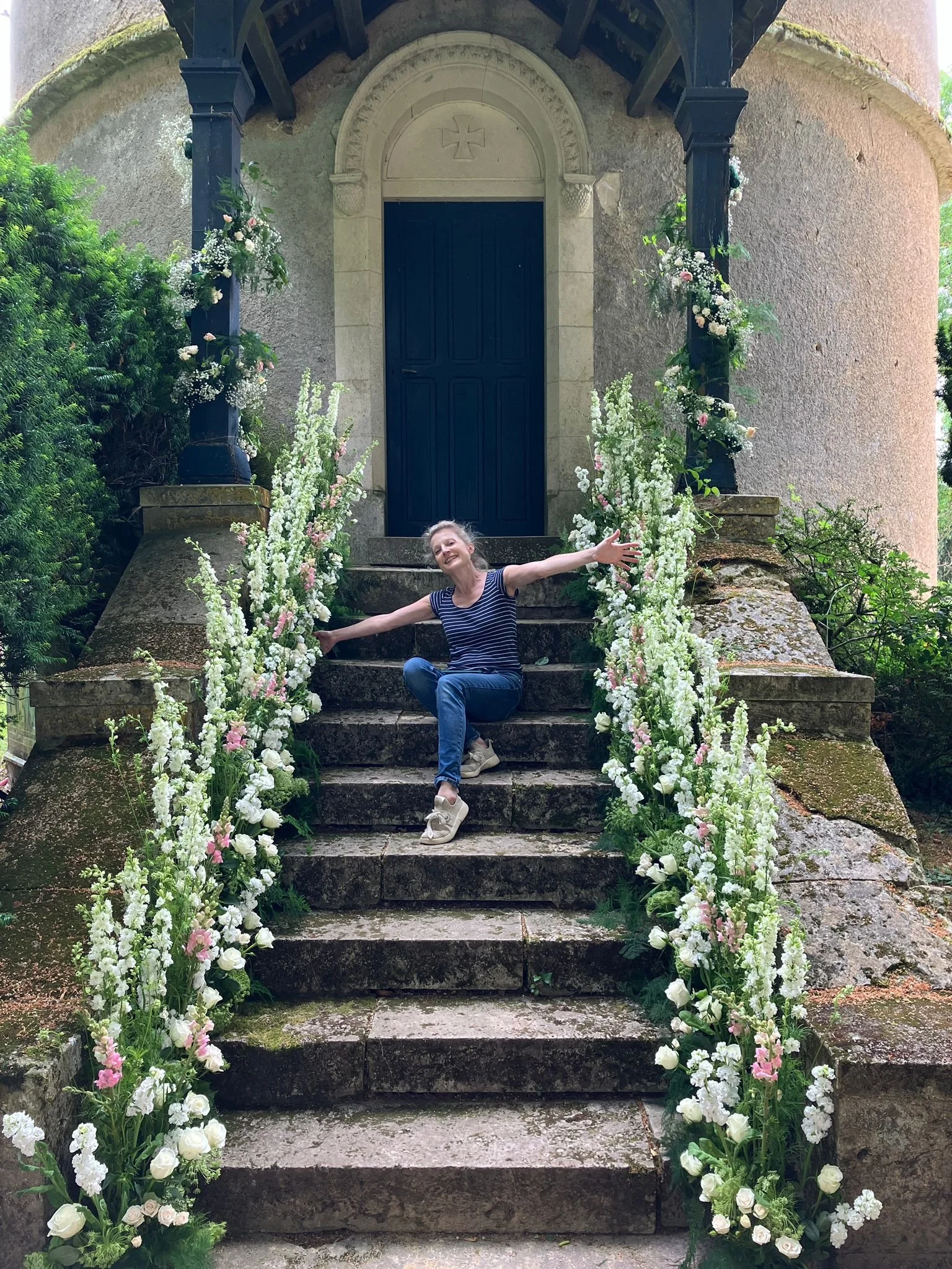 florist sitting on the steps of a french chapel showing the flower arrangements that line the sides of the stairs