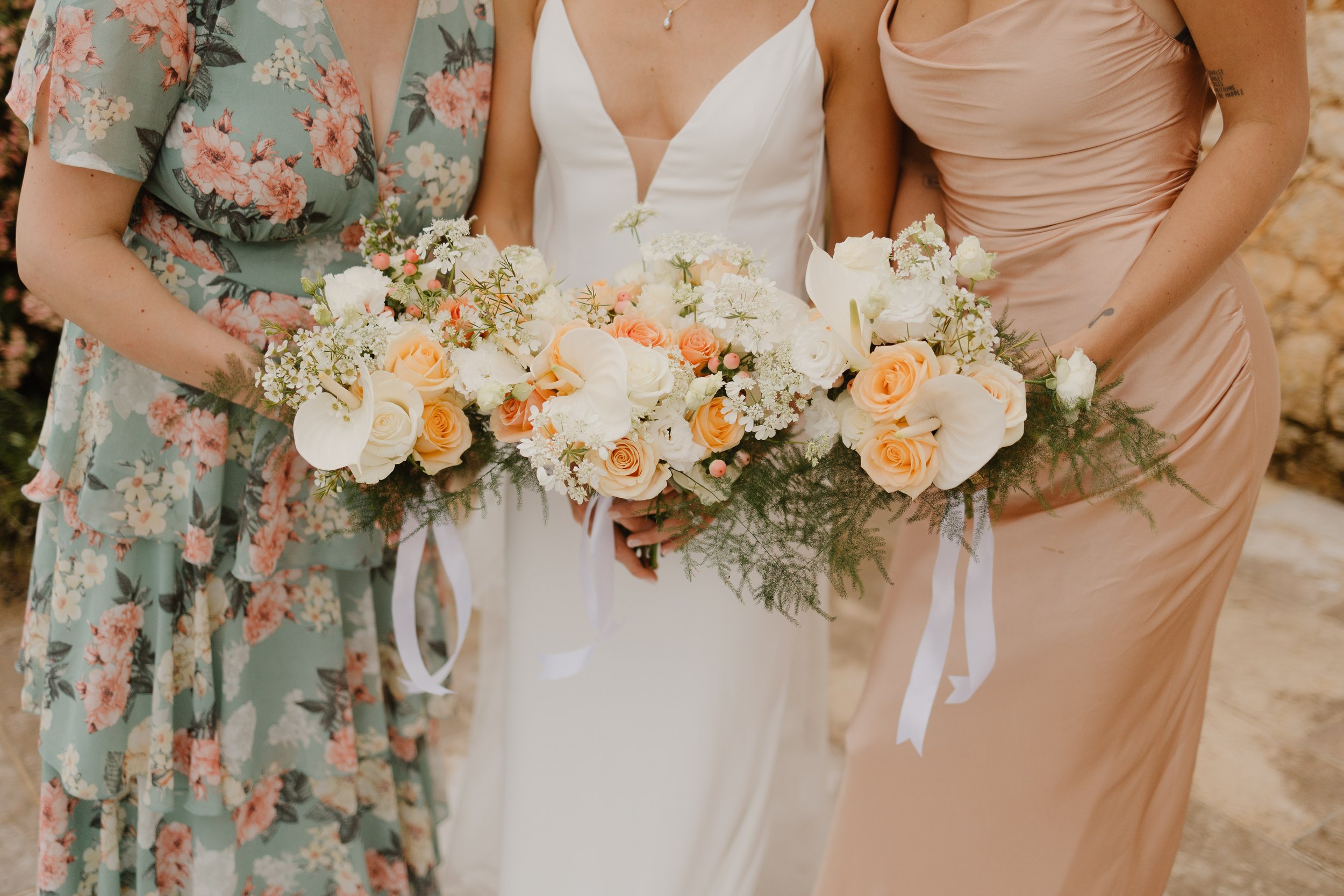 Bridesmaids and the bride hold their bouquets of peach and white flowers in a row at a chateau in france for her destination wedding in france