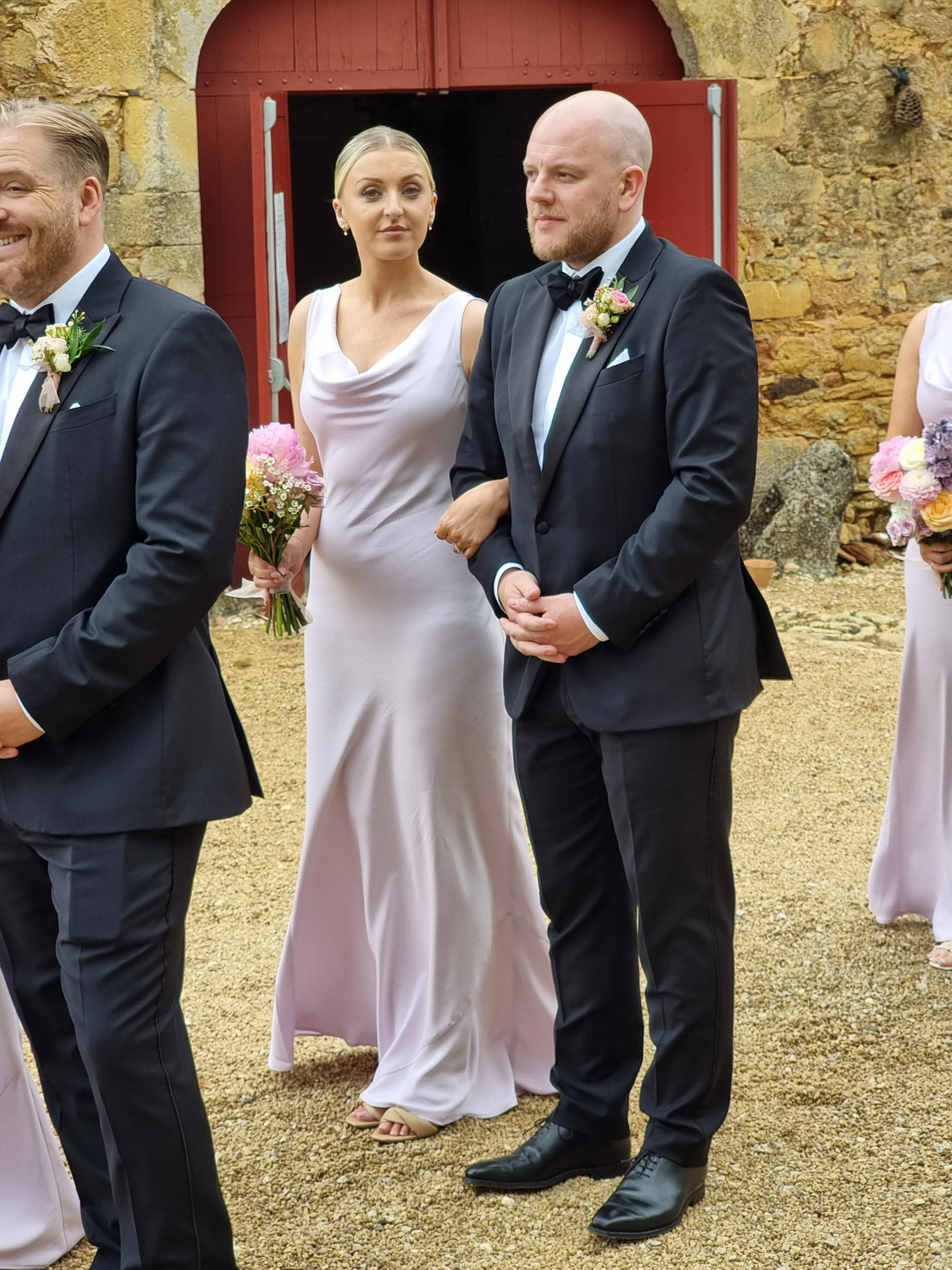 a bridesmaid in a lavender dress holds a floral bouquet standing next to a man dressed in a formal suit at a chateau wedding in france.
