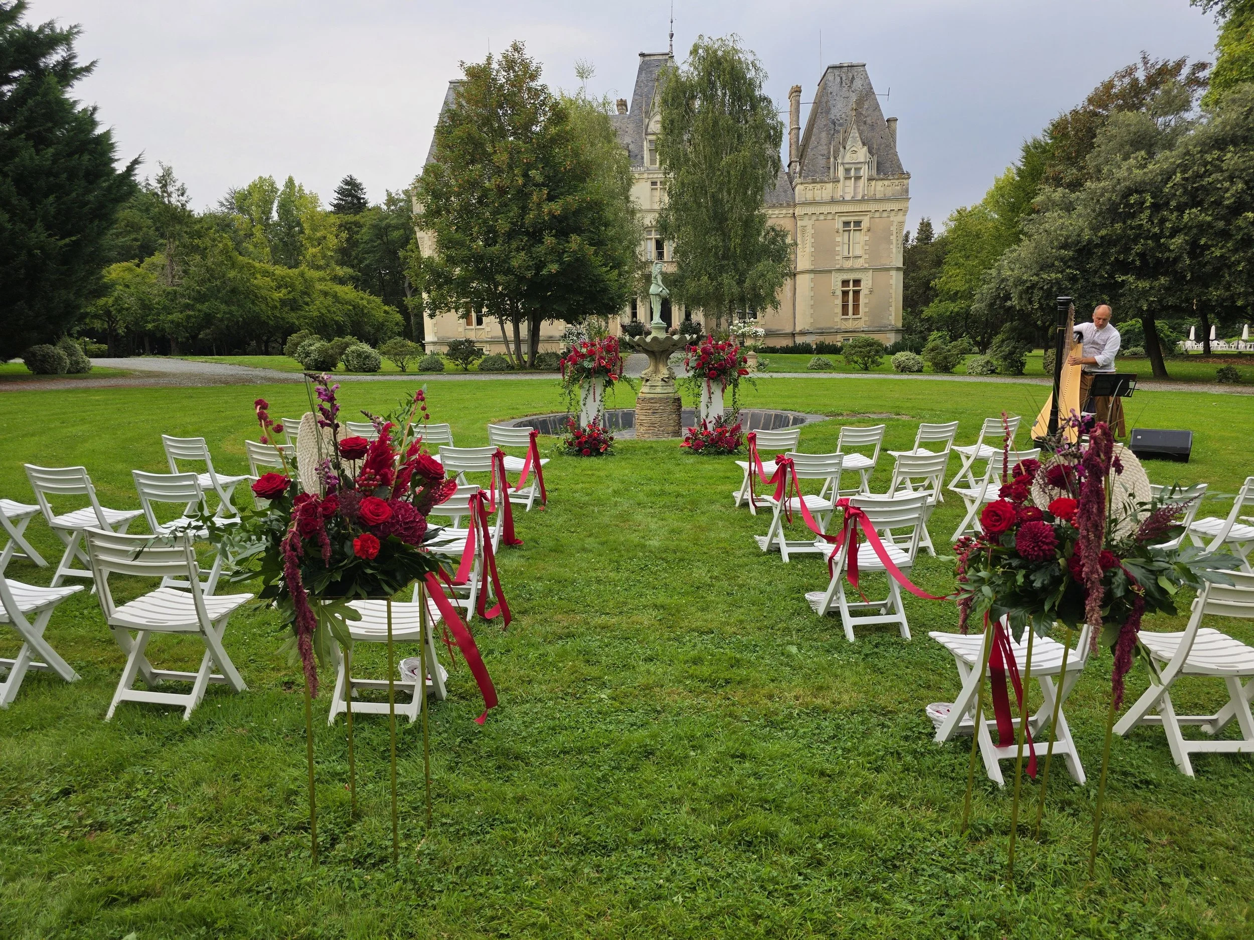 Wedding ceremony aisle with red florals lining the aisles and red ribbon with a view of the chateau in the background. Wedding florist in France