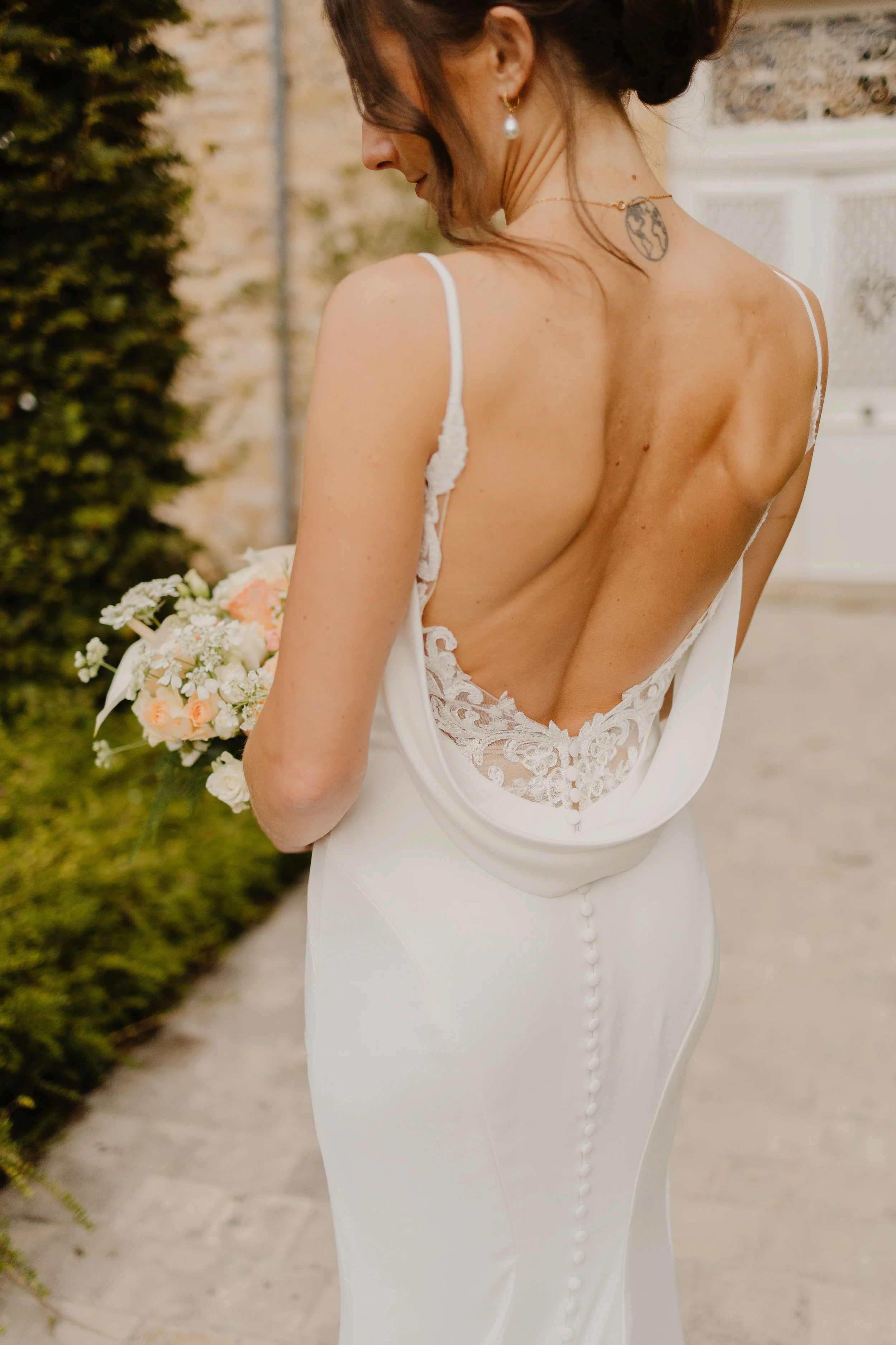 Bride photo shot from behind her as she holds her wedding bouquet in whites and peach colors