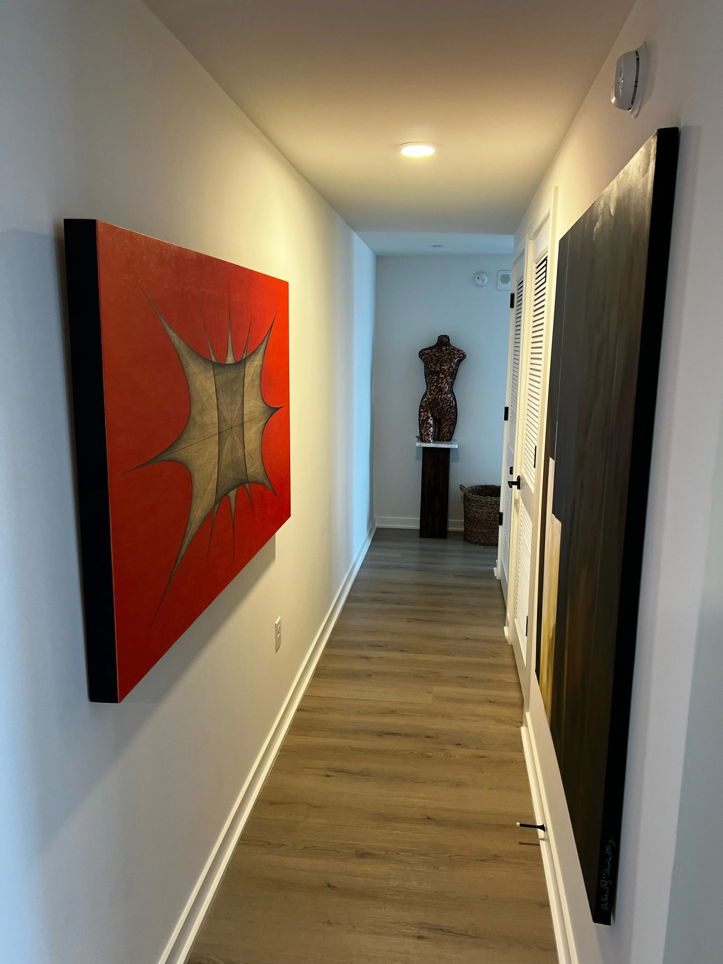A hallway decorated with abstract paintings on the walls and a sculpture of a female torso on a pedestal at the end.